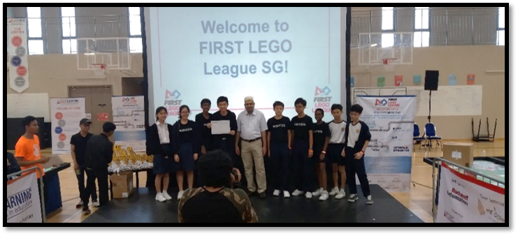 Group of students and an adult on stage at a First Lego League SG event, posing with a certificate.