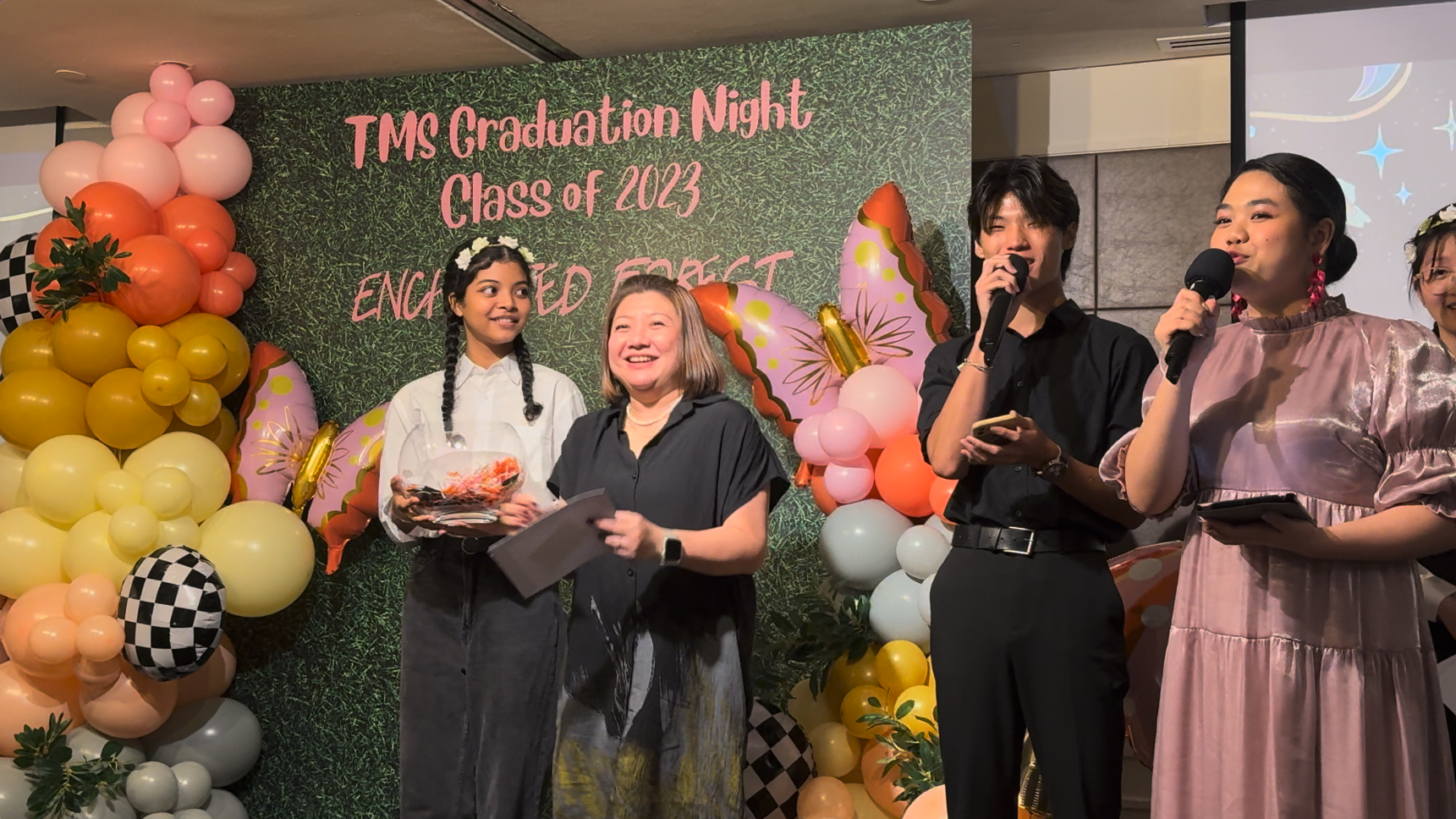 Four people stand before a balloon-decorated backdrop reading TMS Graduation Night Class of 2023 Enchanted Forest.