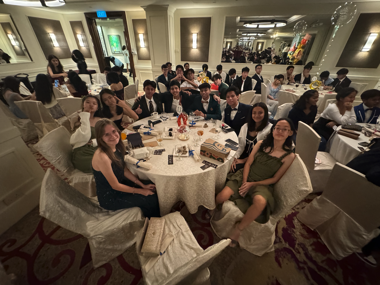 Teenagers in formal attire sit at round tables in a banquet hall during what appears to be a school prom.