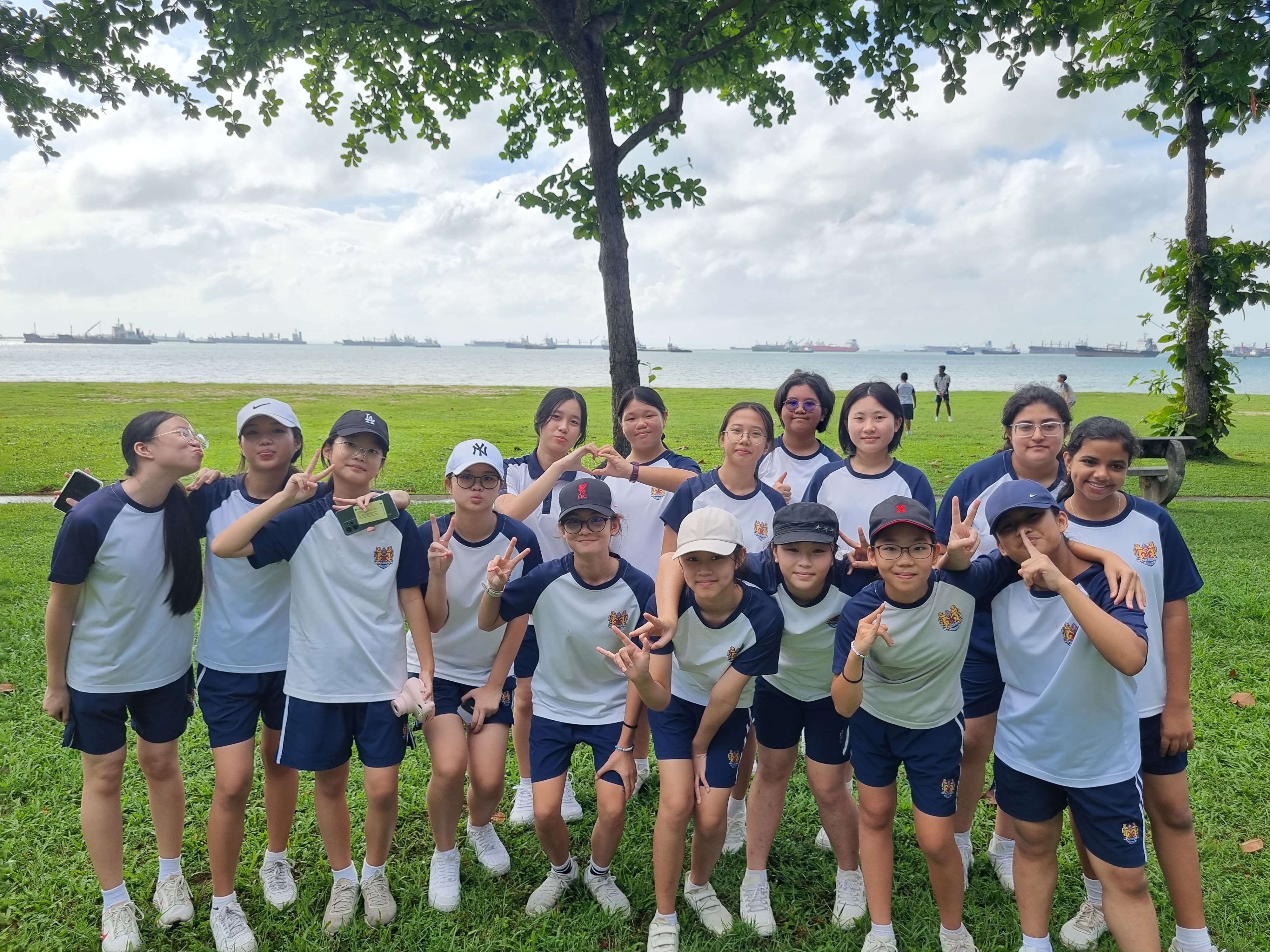 A group of teenage students in matching blue and white uniforms pose with peace signs near a waterfront park.