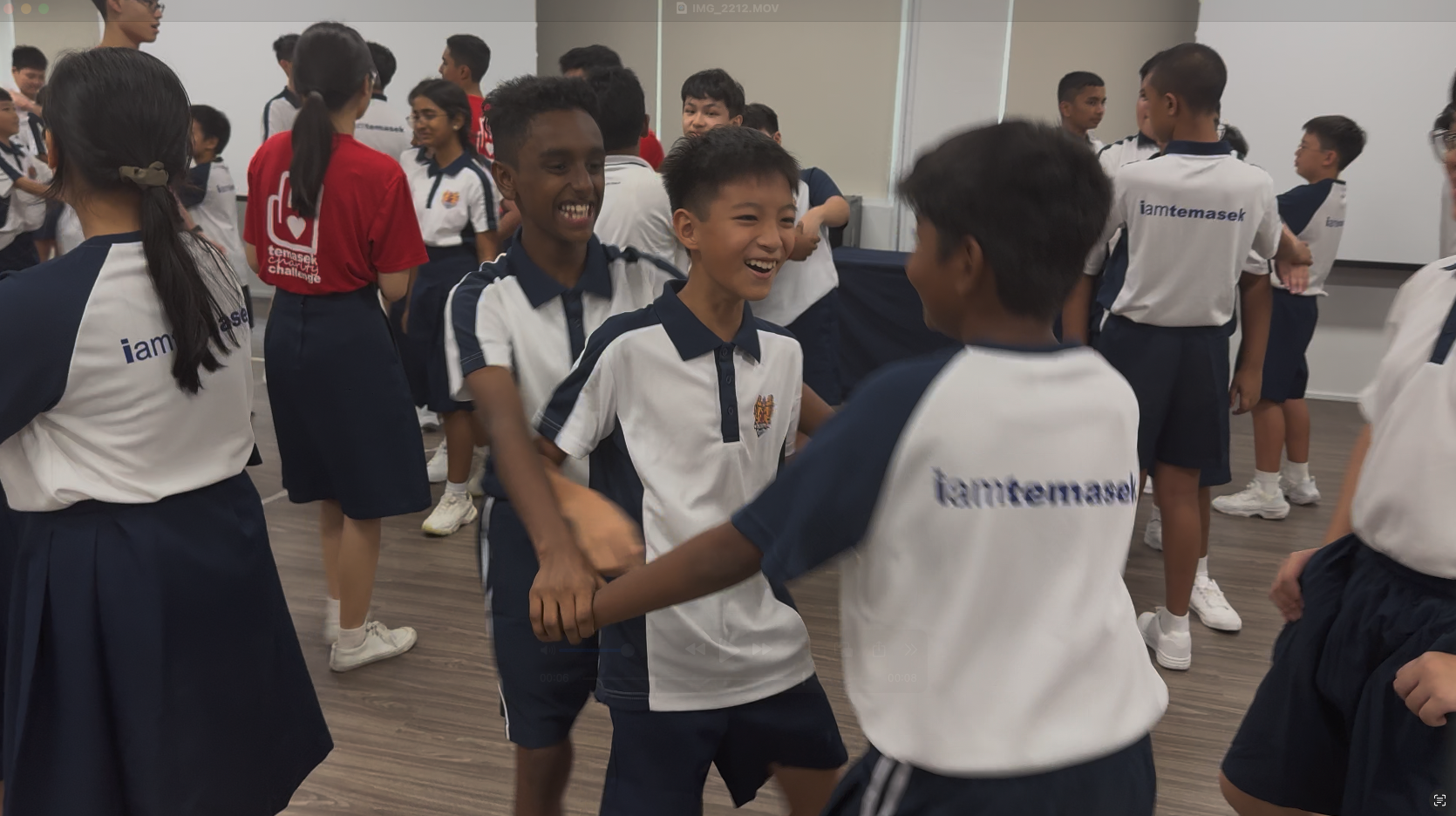 Students in school uniforms and iamtemasek shirts laugh and interact in an indoor activity session.