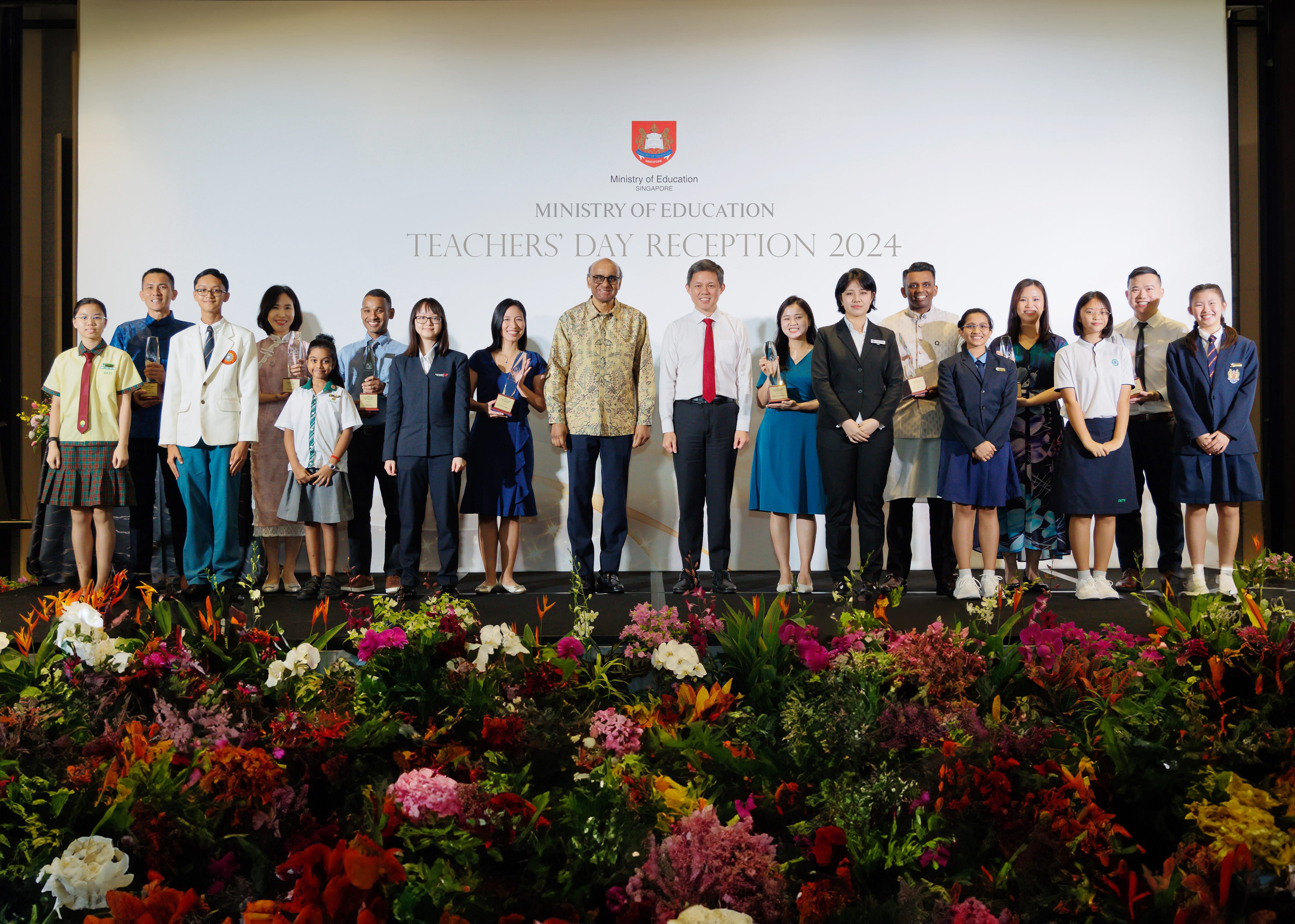 Group of people posing on stage at the Ministry of Education Teachers' Day Reception 2024, with flowers in front.