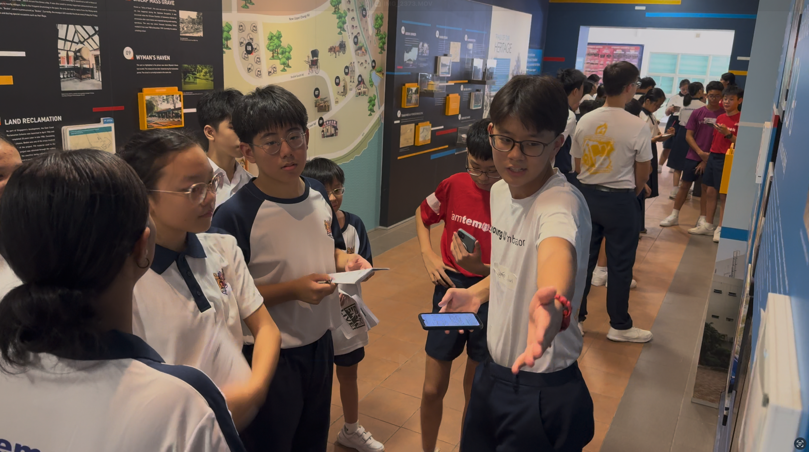 Students in school uniforms explore a museum exhibit with historical maps and information panels on the walls.