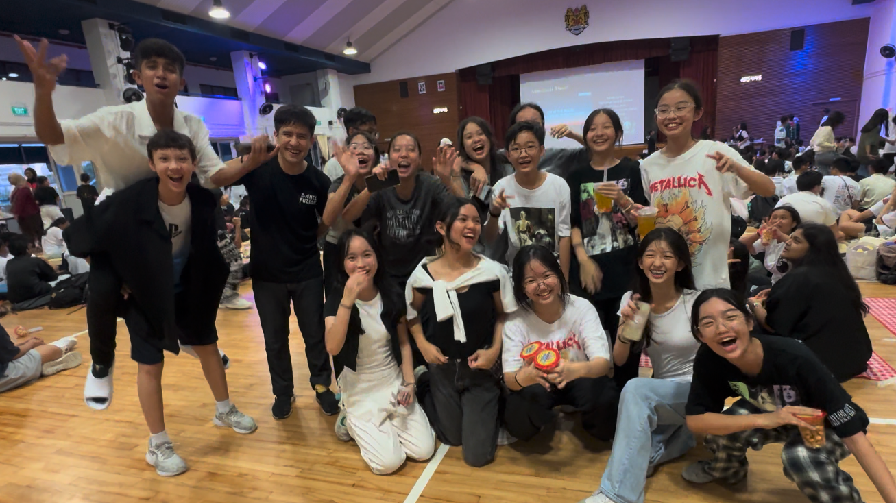 A large group of cheerful young people pose together in a school hall during a lively indoor event.