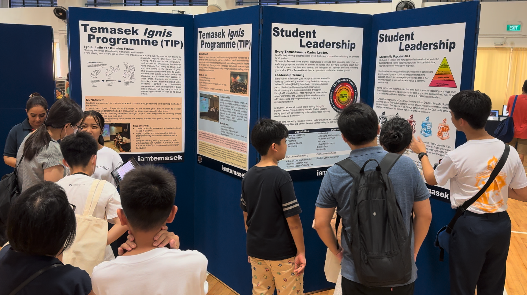 Students gather around display boards showing Temasek Ignis Programme and Student Leadership information at a school fair.