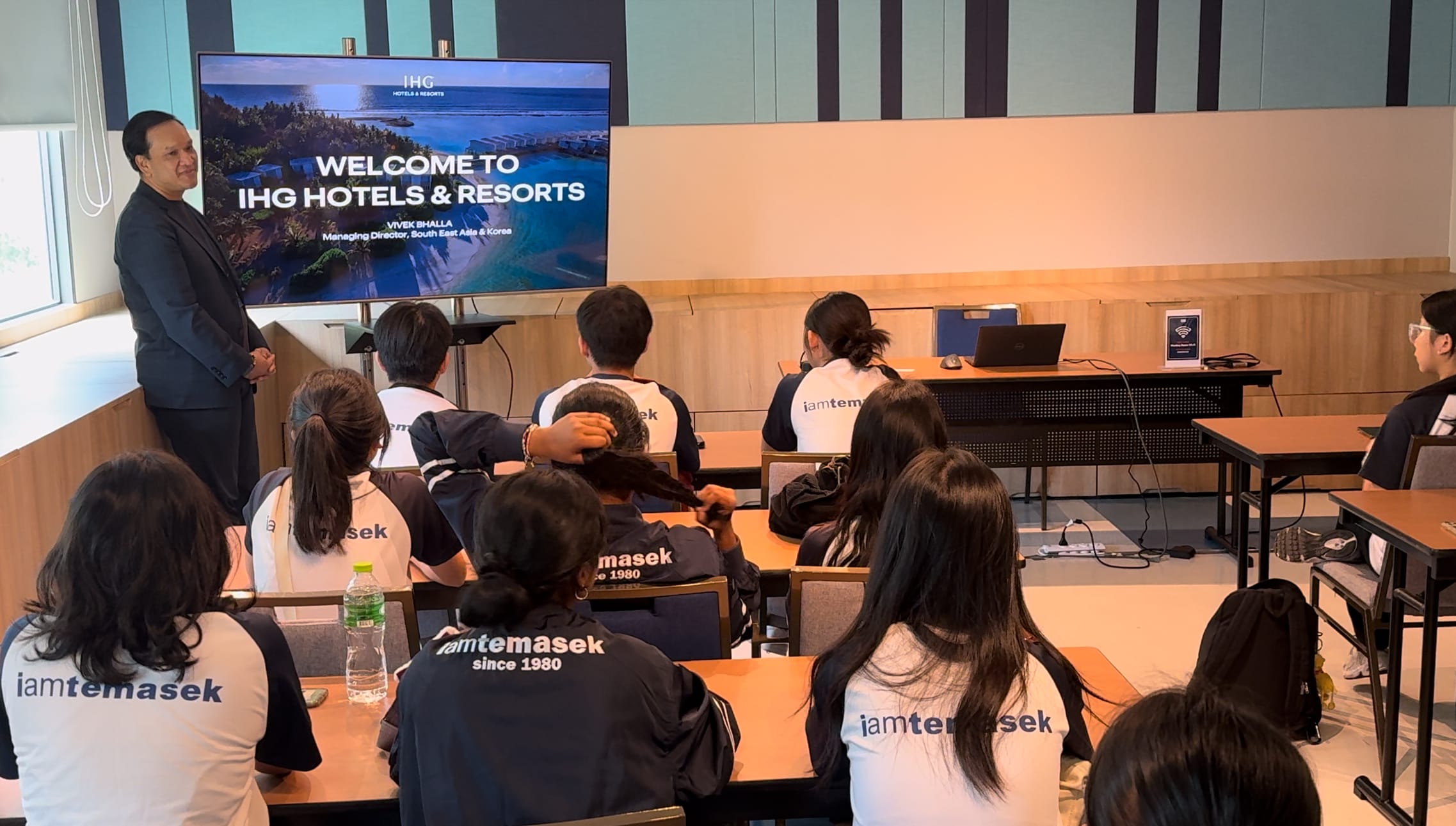 A man presents an IHG Hotels and Resorts slide to students in Temasek uniforms seated at desks.