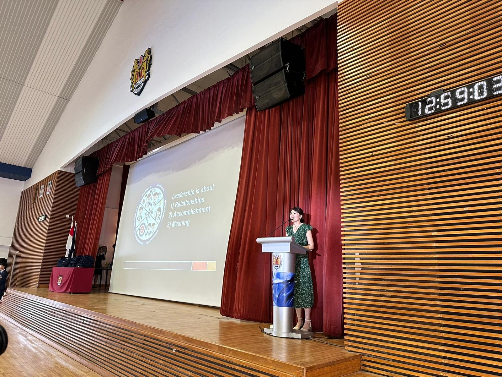 Woman in green dress speaking at a podium on a stage with a projected slide about leadership.