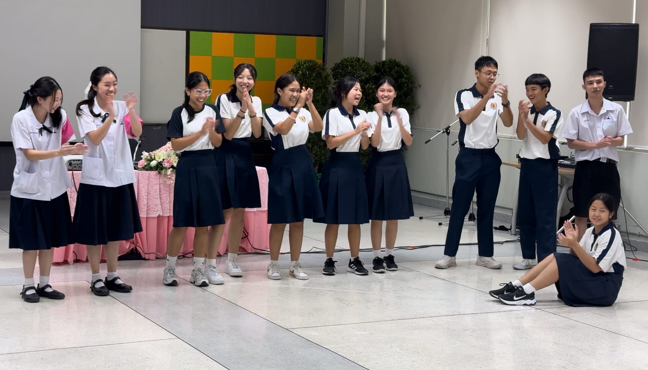 A group of uniformed students clapping and smiling together on a stage during a school event.