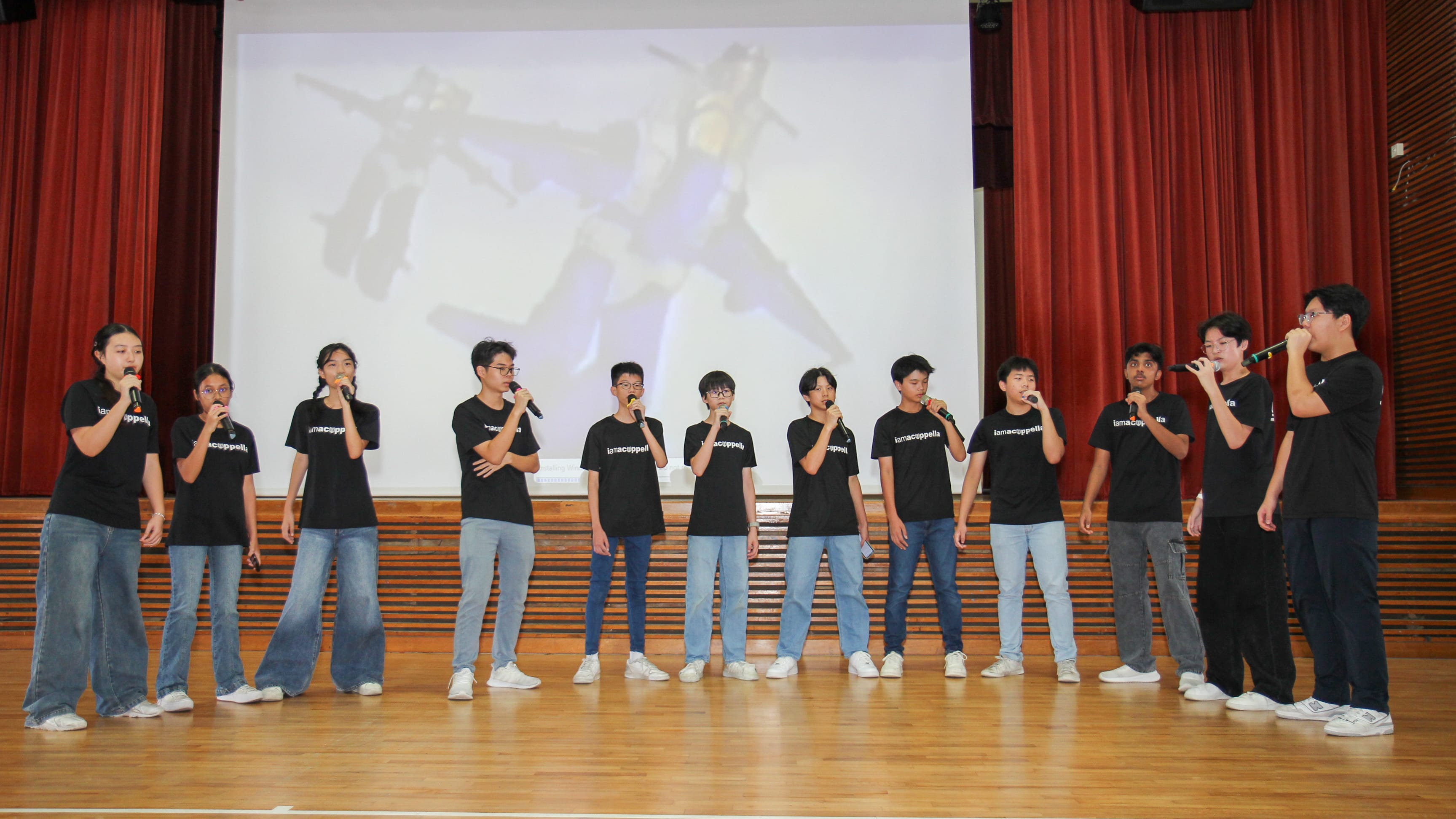 Eleven youths on stage in black shirts and jeans, singing into microphones before a large screen.