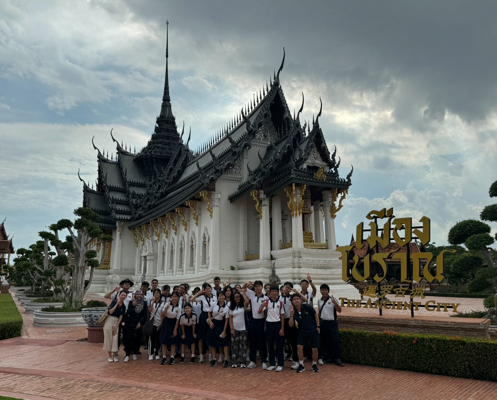 A group of students in uniforms poses in front of a white and black Thai temple at The Ancient City.