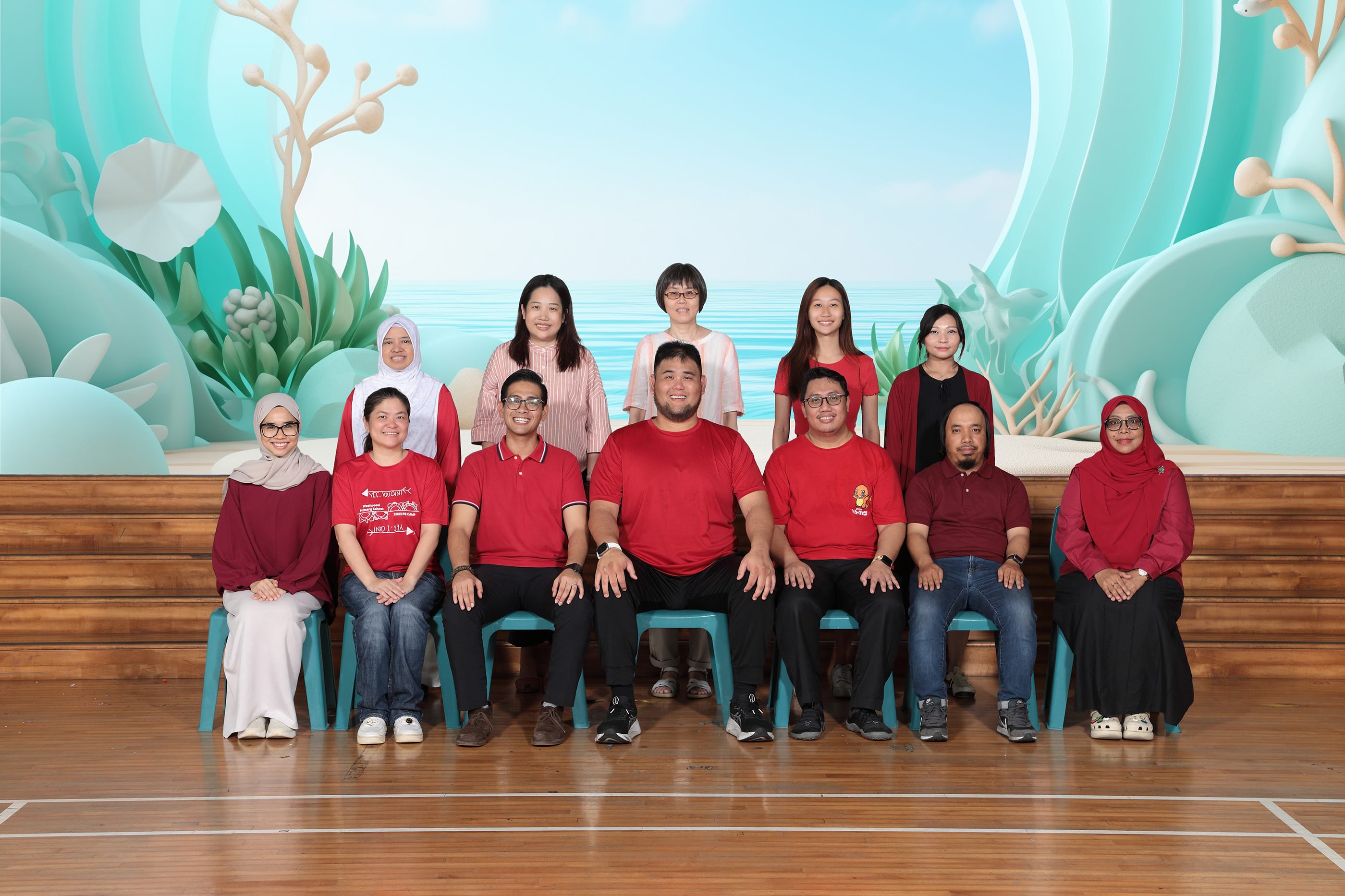 Group of 12 people posing for a photo, front row seated, back row standing, before a teal ocean-themed backdrop.