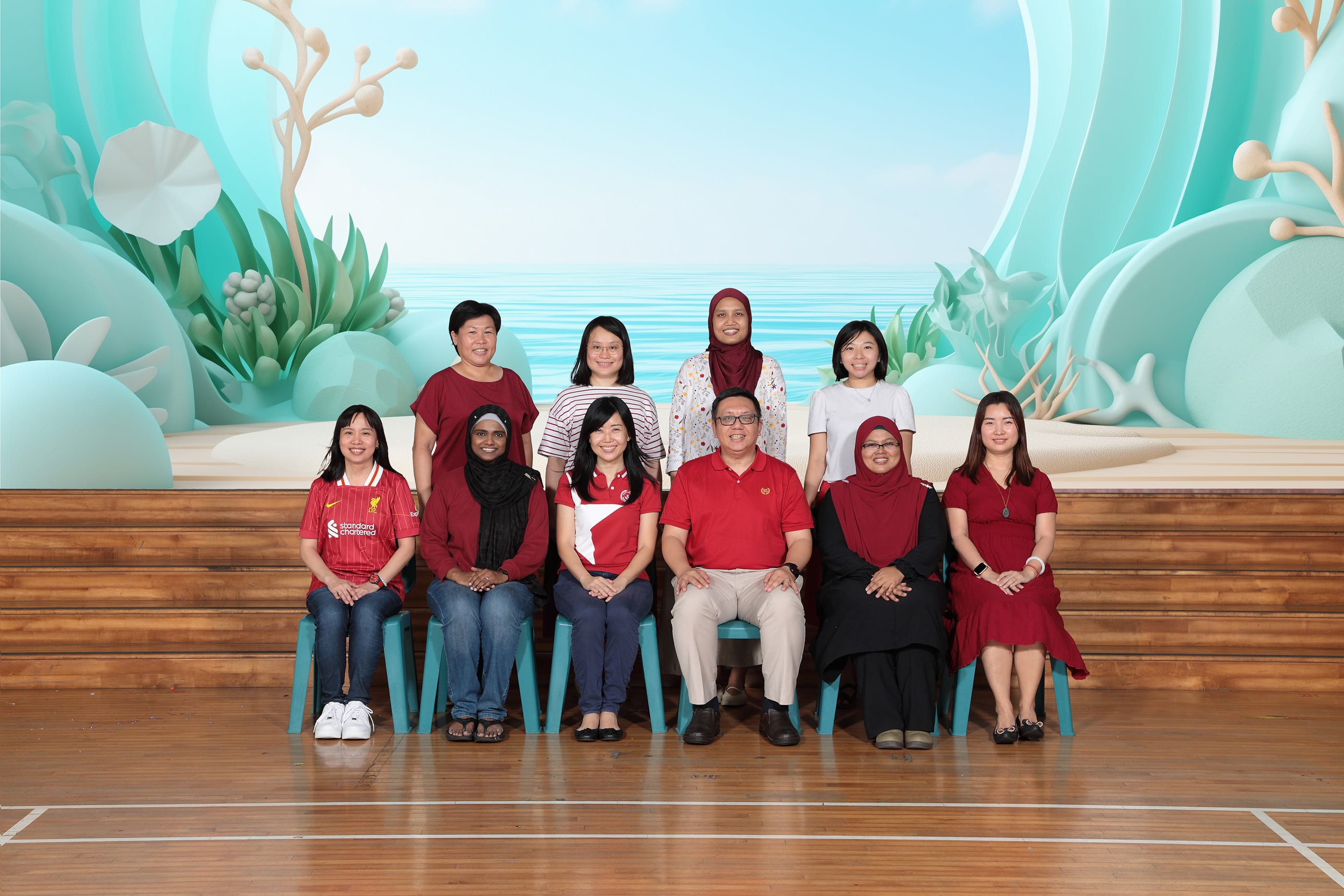 Ten adults pose for a group photo in two rows against a teal ocean-themed decorative backdrop.