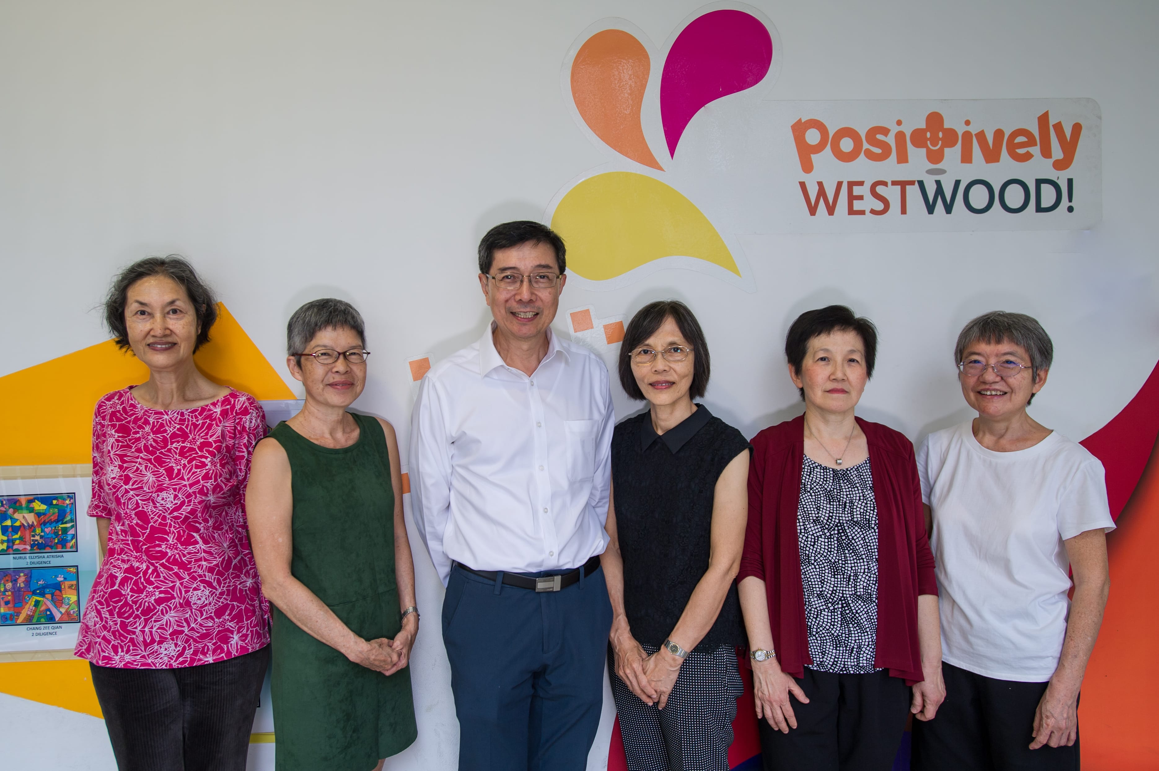 Six adults pose indoors against a wall with colorful shapes and a Positively Westwood! sign.