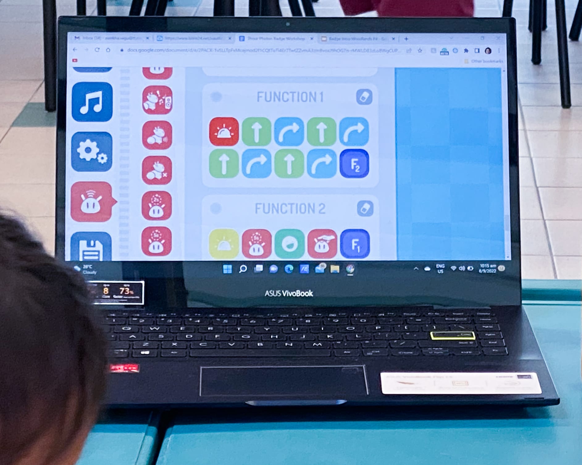 ASUS VivoBook laptop showing a coding interface with Function 1 and Function 2 blocks containing colorful arrow icons.