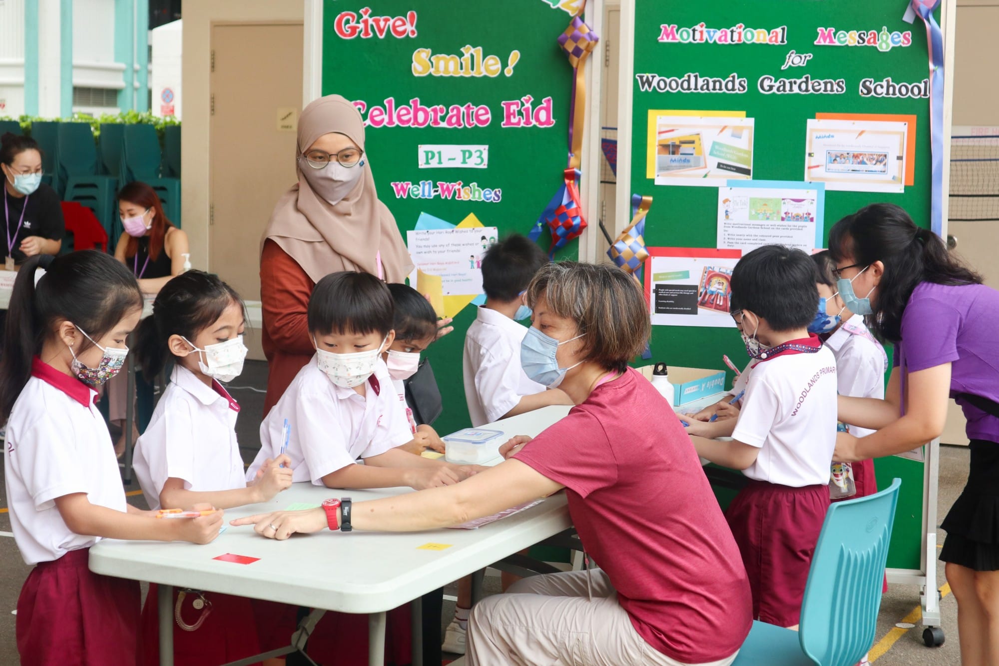 Children in school uniforms and masks write well-wishes at a table during a Celebrate Eid event at Woodlands Gardens School.