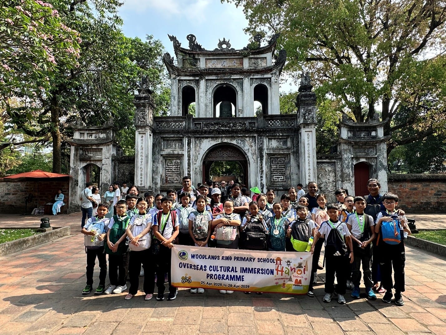 Students and teachers from Woodlands Ring Primary School pose with their programme banner in front of the grand stone entrance gate of the Temple of Literature in Hanoi.