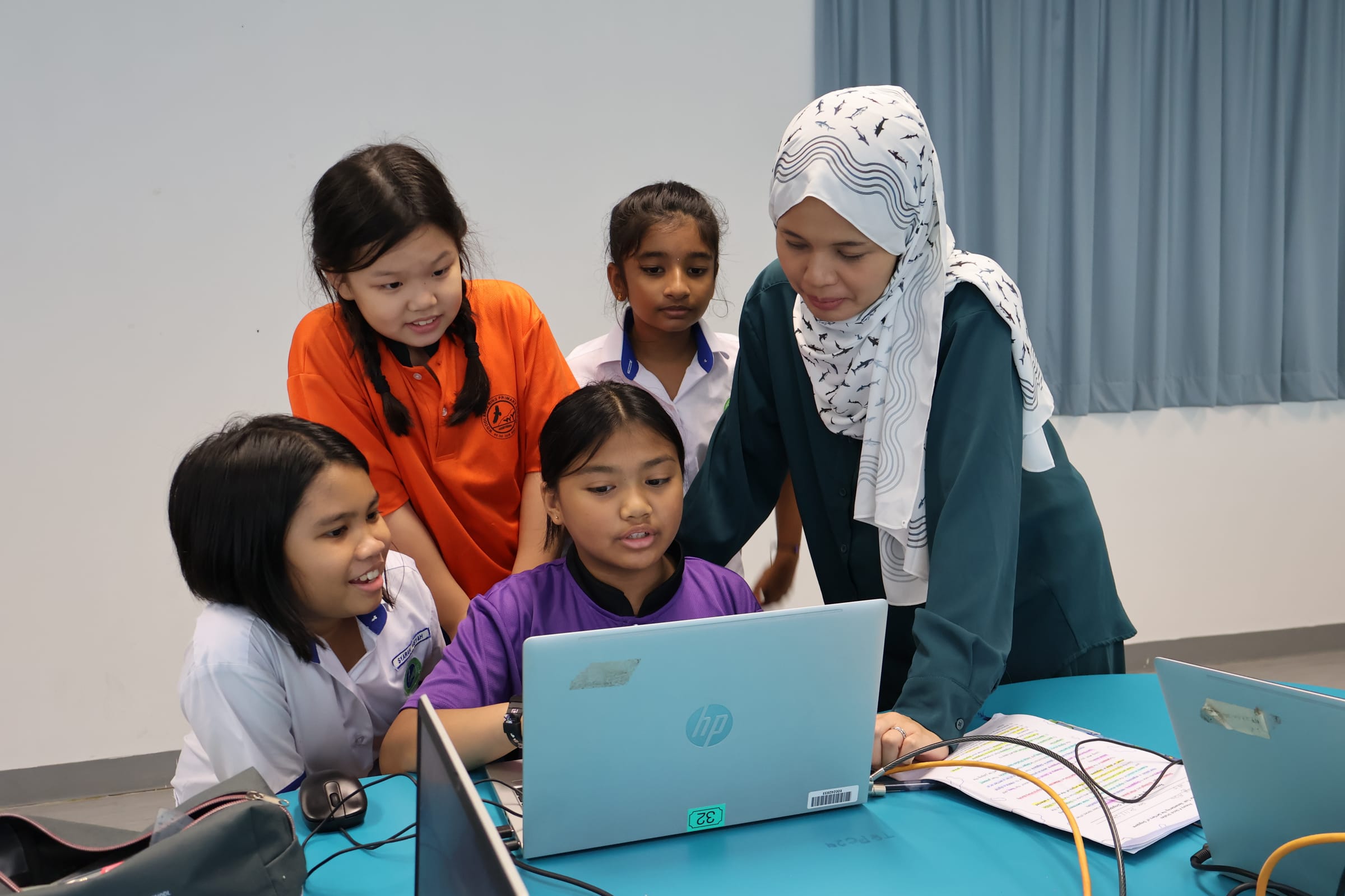 teacher guiding four students gathered around an HP laptop during an ICT lesson
