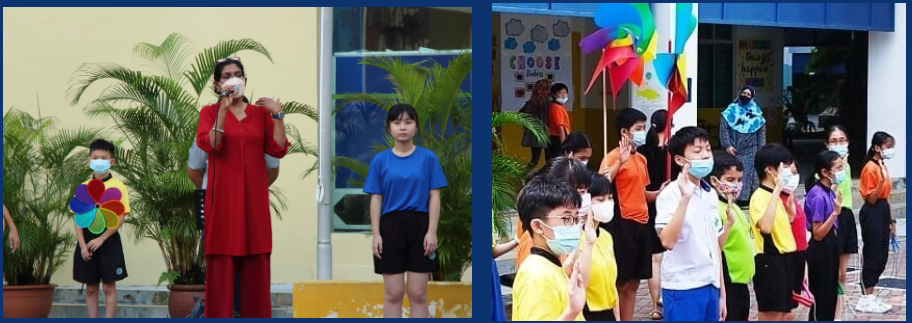 A teacher speaks into a microphone while masked students stand outdoors; another group of masked children raises hands nearby.