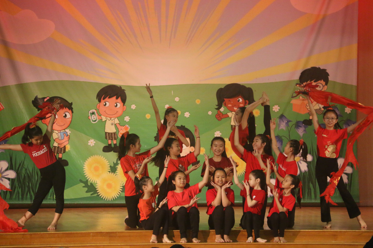Photograph of Chinese Dance students performing at the school's Chinese New Year concert. The students wear matching red costumes and perform a choreographed dance with flowing red ribbons.