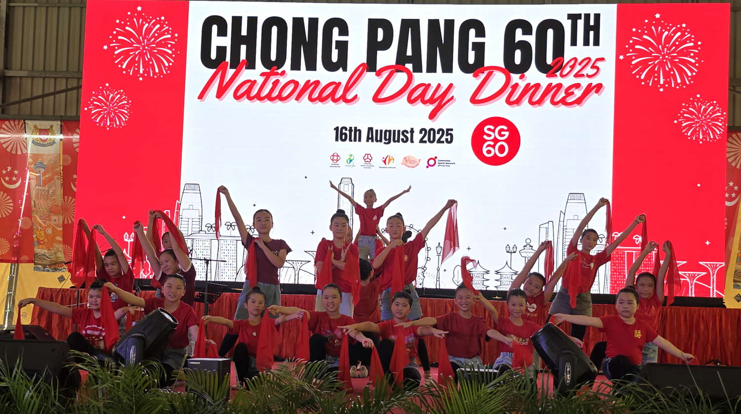Photograph of Yishun Primary School's Chinese Dance students performing at the Chong Pang 60th National Day Dinner 2025 in celebration of SG60. The students wear matching red costumes and perform a choreographed dance with flowing red ribbons on stage.