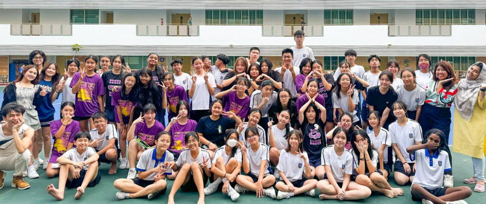 Large group of students in white and purple shirts posing together outdoors in front of a school building.