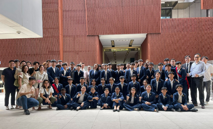 Large group of students in navy uniforms posing for a photo in front of a modern red brick building.