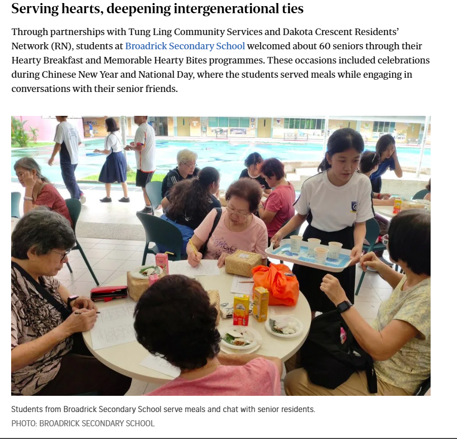 A student in uniform carries a tray of drinks to elderly seniors seated at a round table outdoors.