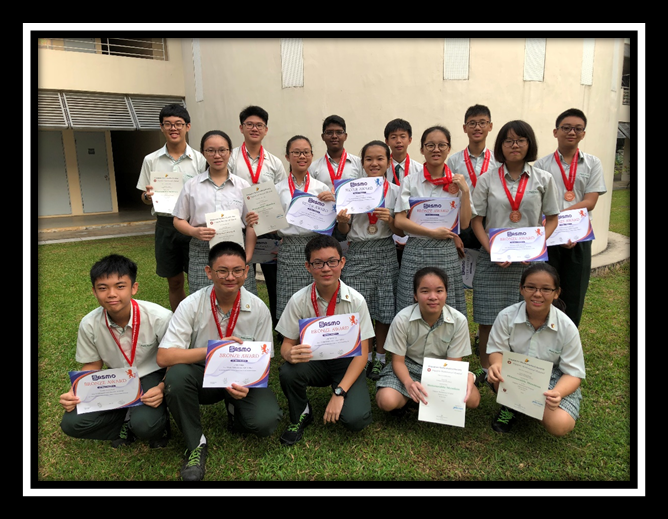 A group of school students in uniform wearing medals and holding certificates outdoors on grass.