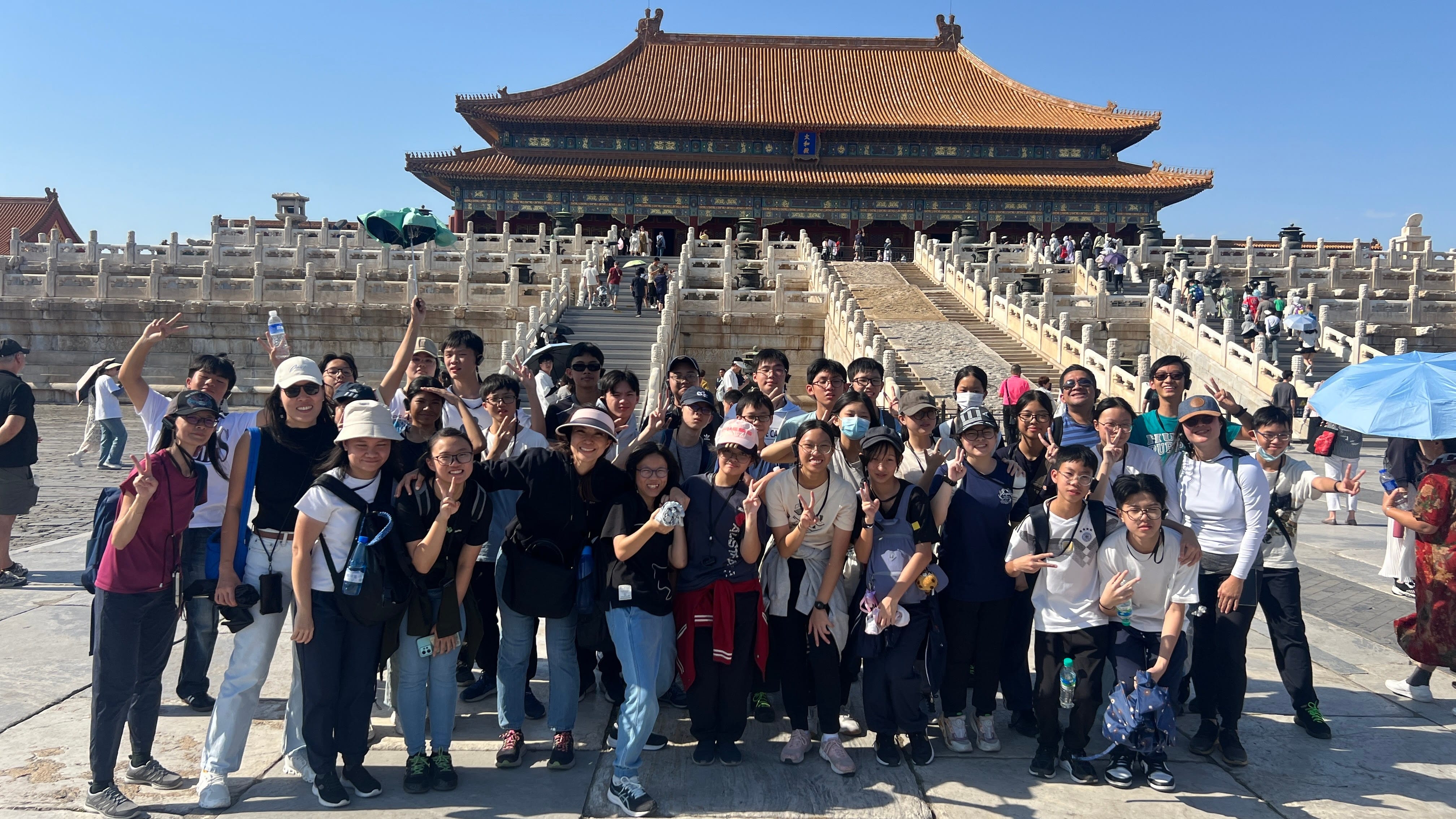 A large group of young people pose with peace signs in front of the Forbidden City's main hall in Beijing.