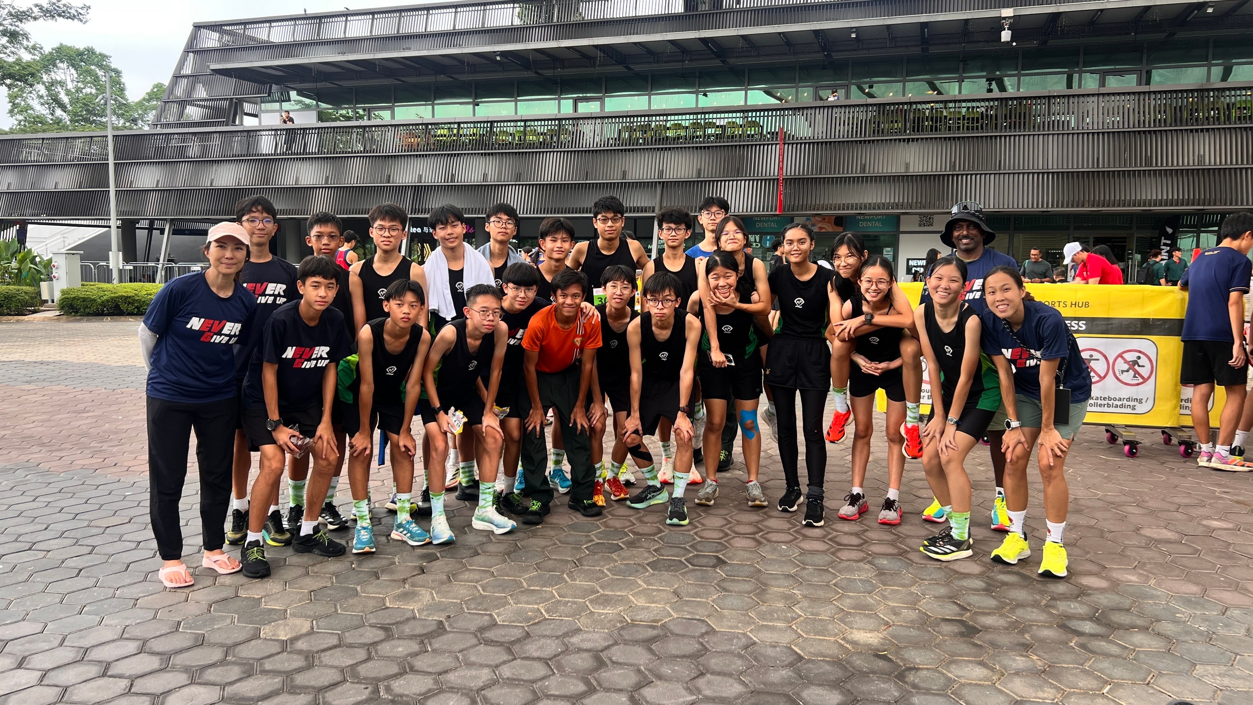 A large group of young athletes in black uniforms pose together outside a sports hub building.