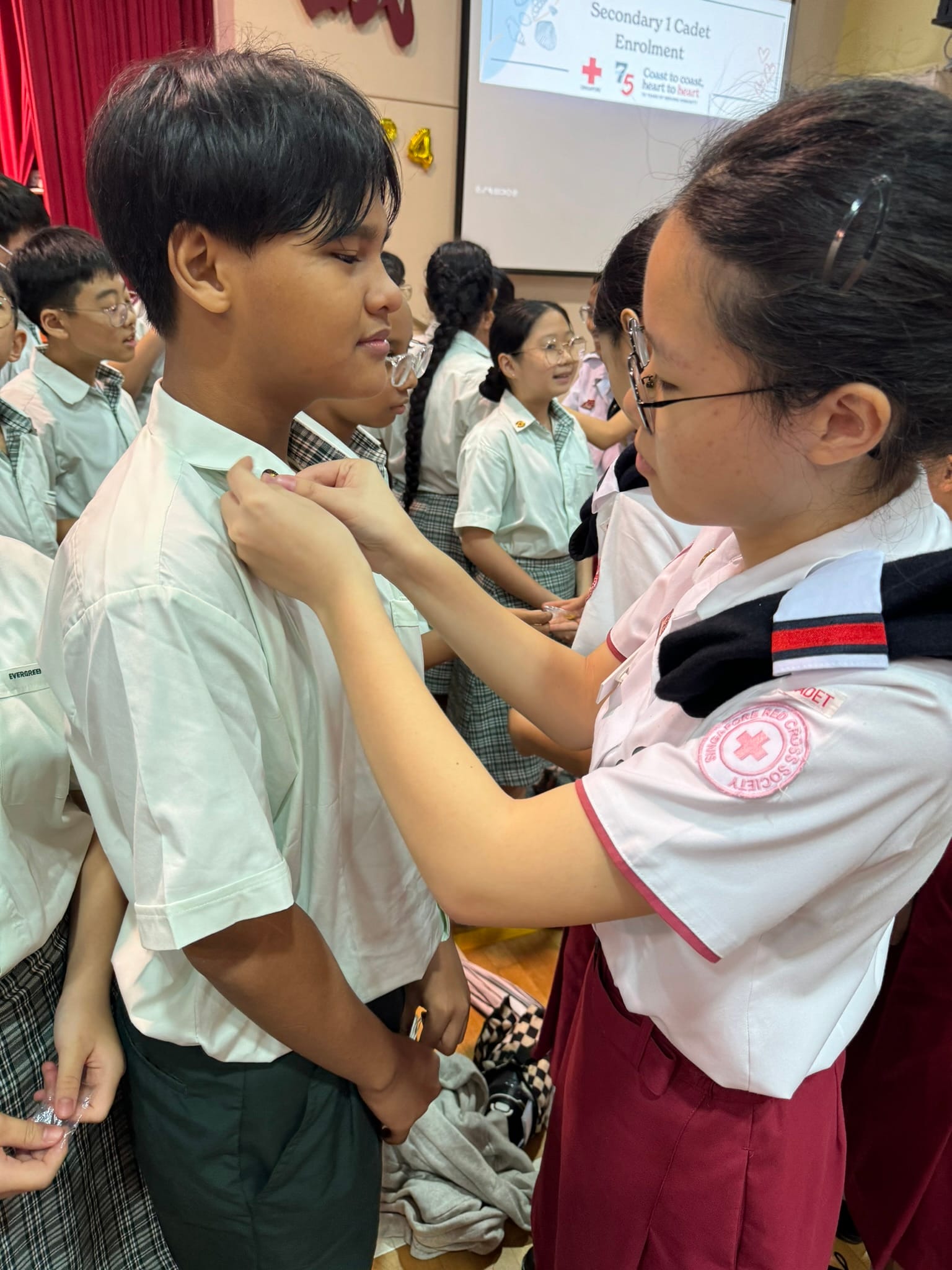 A Singapore Red Cross cadet pins a badge on a younger student during a Secondary 1 Cadet Enrolment ceremony.