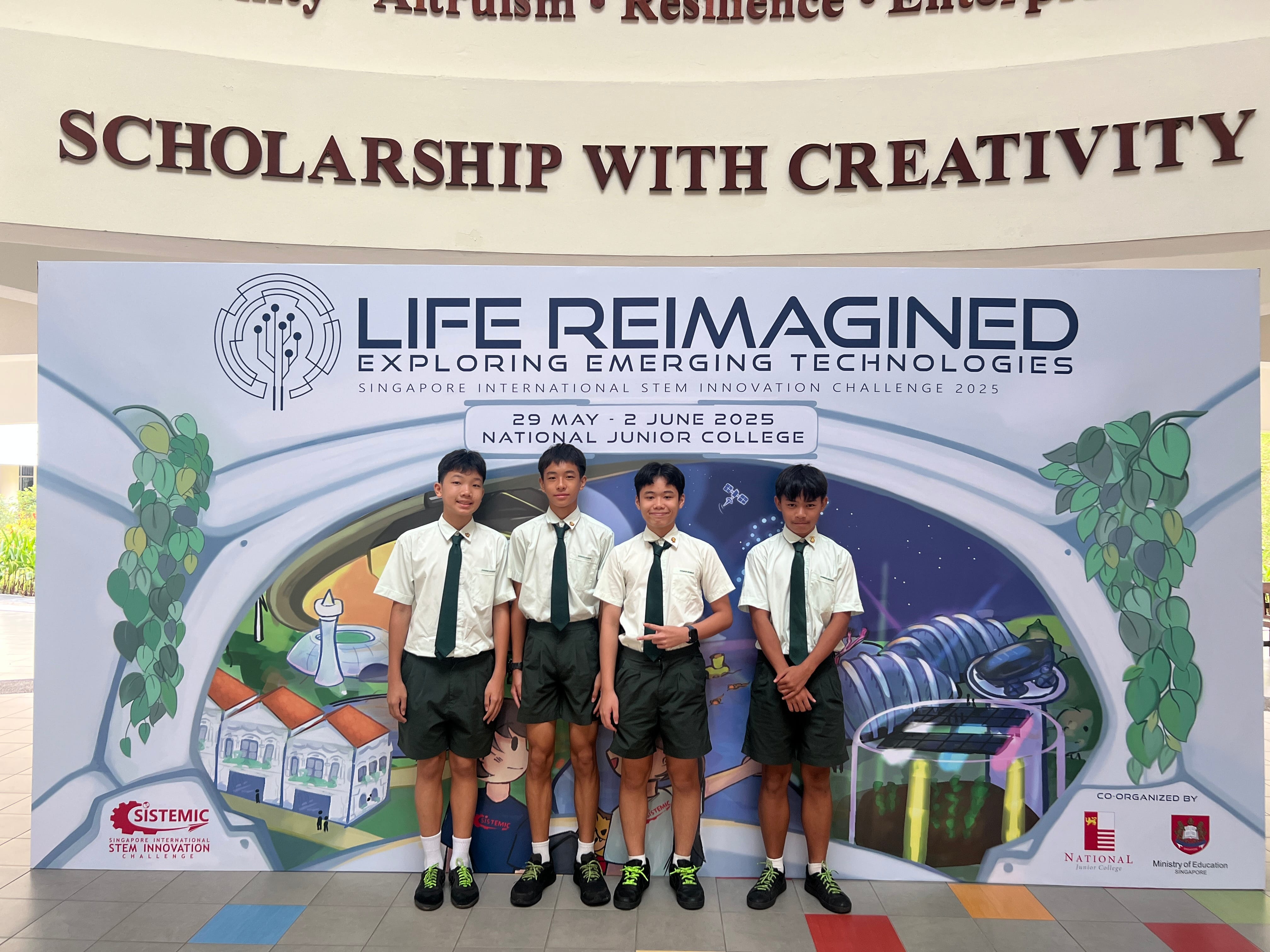 Four male students in white shirts and dark shorts stand before a Life Reimagined STEM Innovation Challenge 2025 banner.