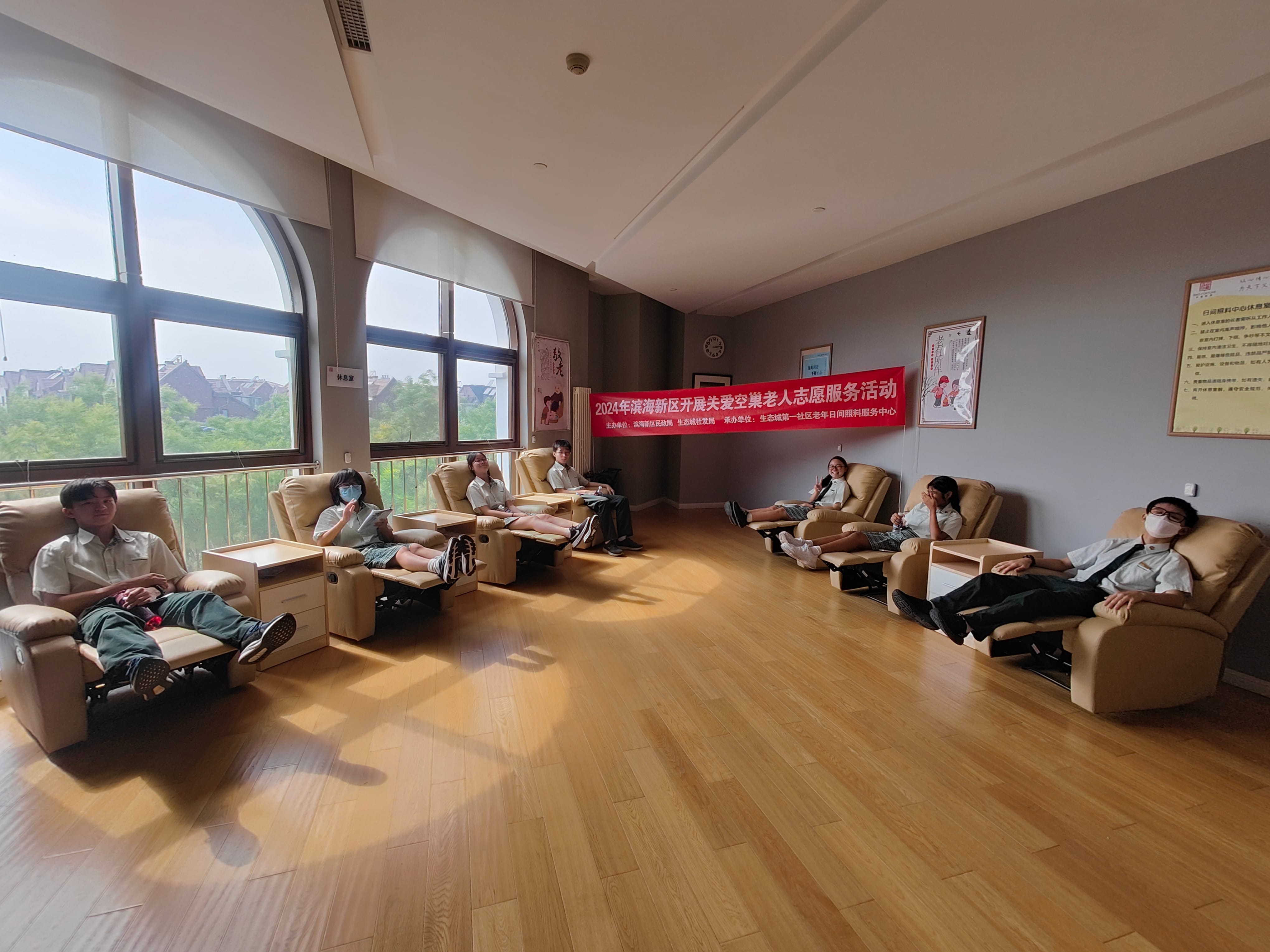Several young people in uniforms sit in recliner chairs in a bright room with a red Chinese banner on the wall.