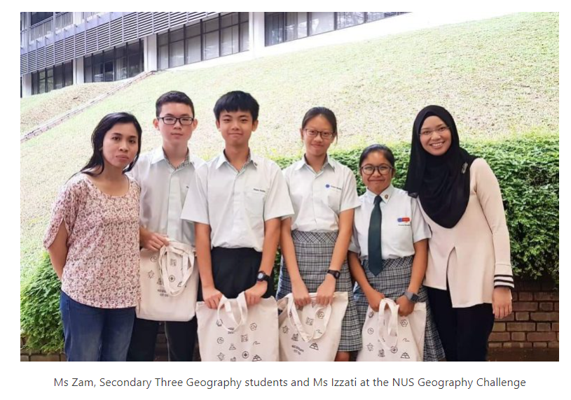Six people in school uniforms and casual wear pose outdoors holding tote bags near a grassy slope and building.