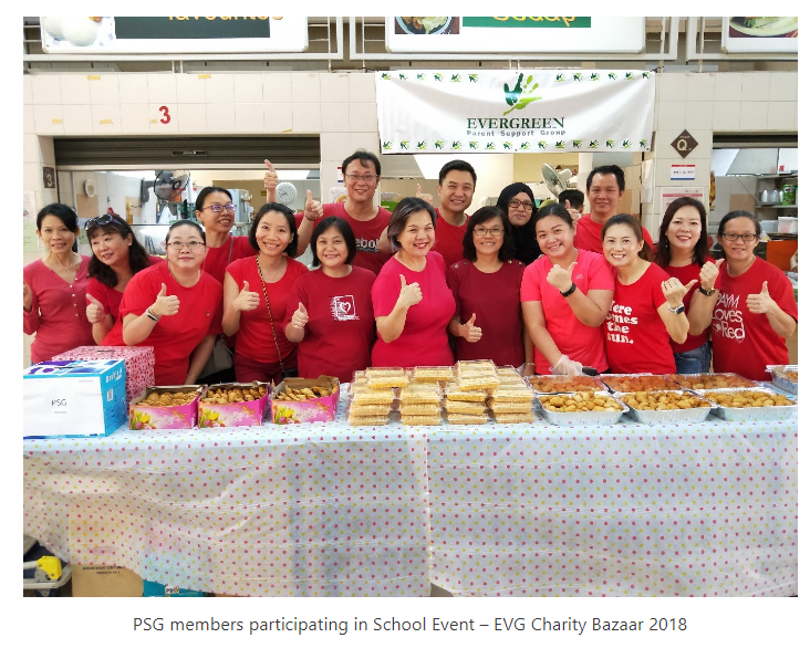 Group of people in red shirts giving thumbs up behind a food table at Evergreen Parent Support Group charity bazaar.