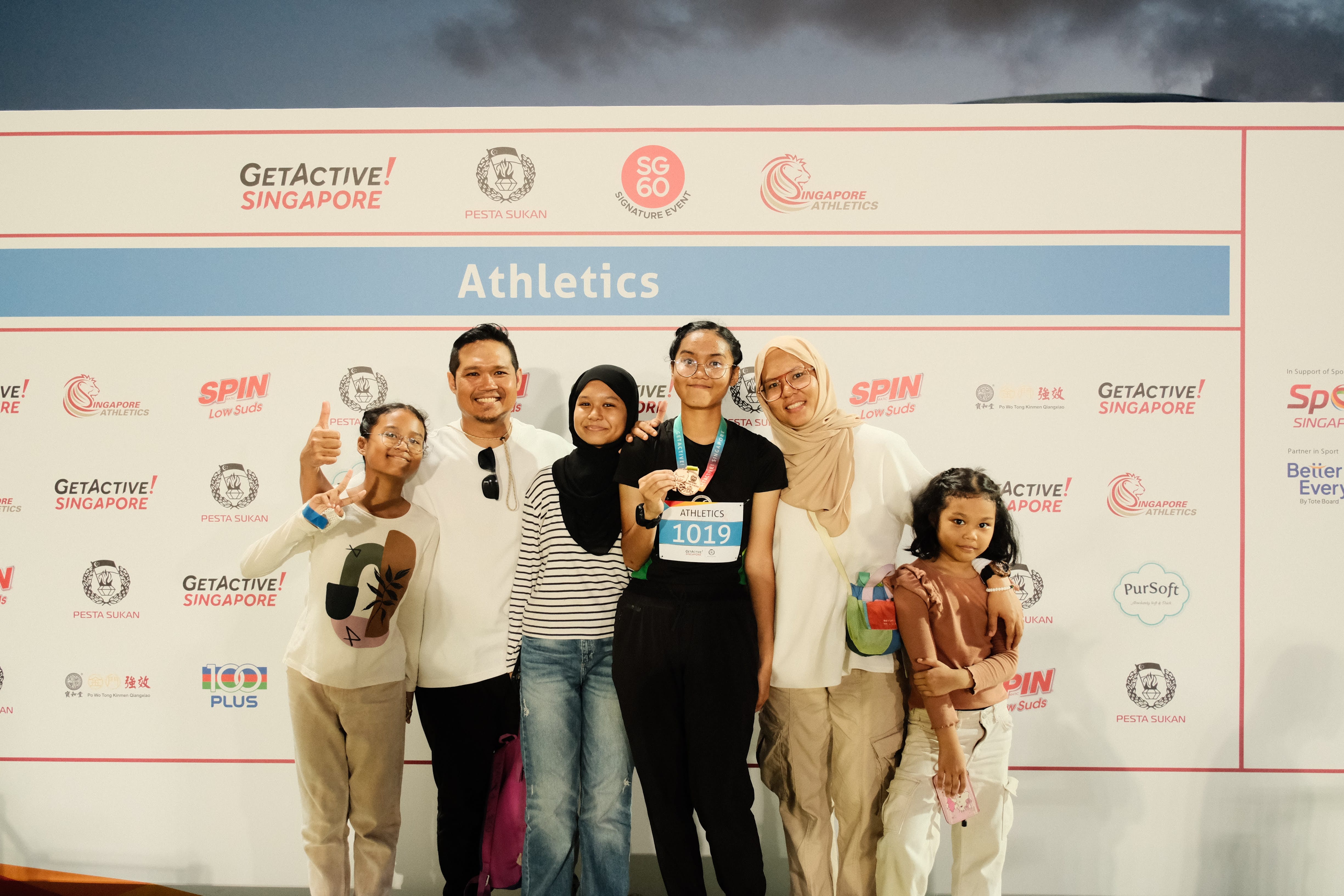 Six people pose in front of a GetActive Singapore Athletics event banner; one person holds a medal with bib number 1019.