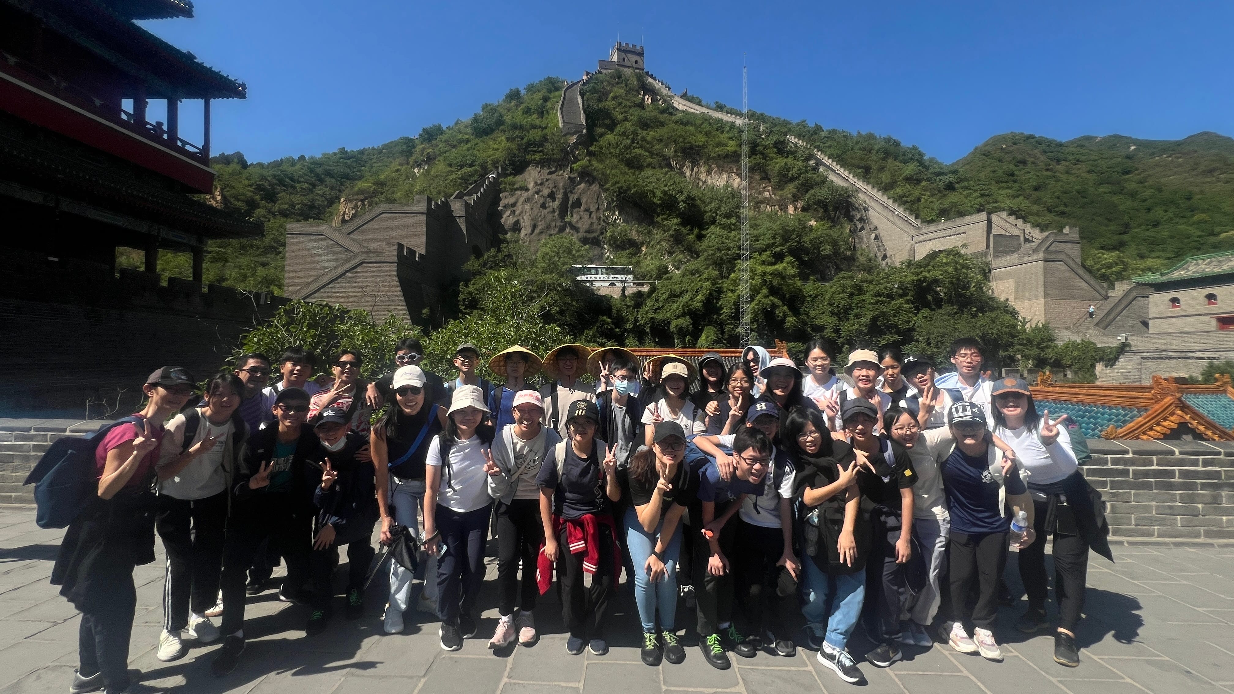 A large group of tourists posing for a photo at the Great Wall of China on a sunny day.