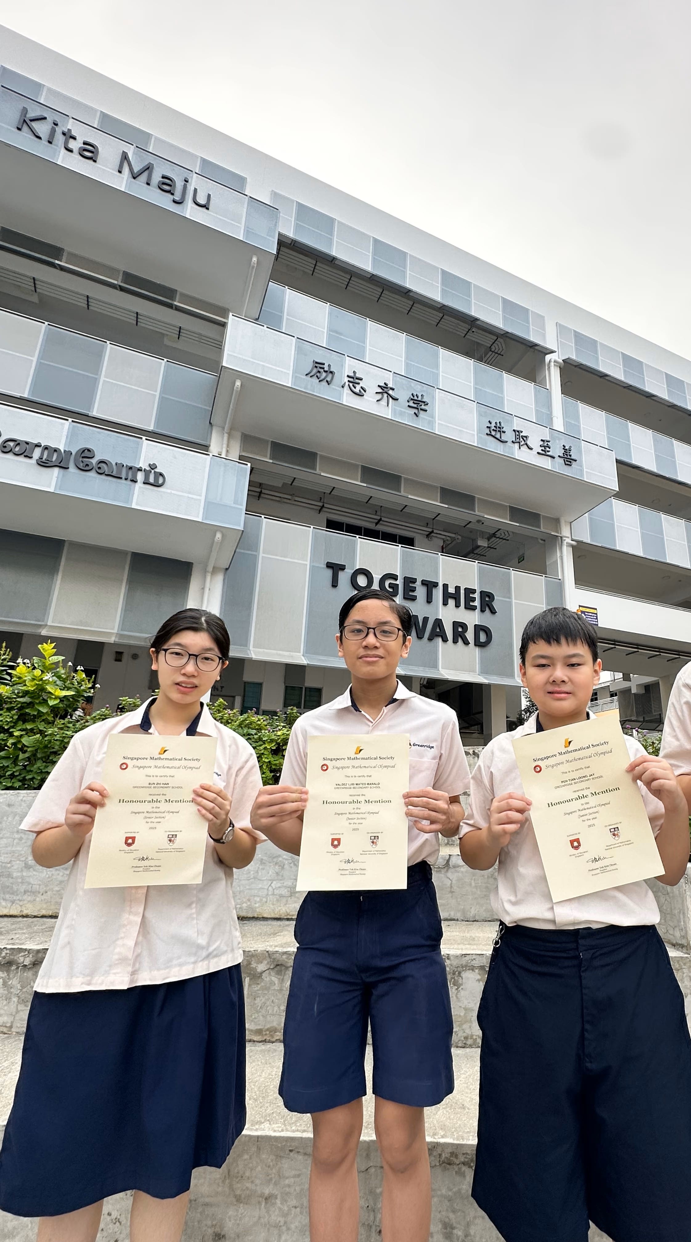 Three students in school uniforms hold Honourable Mention certificates in front of a building reading "Together Forward."