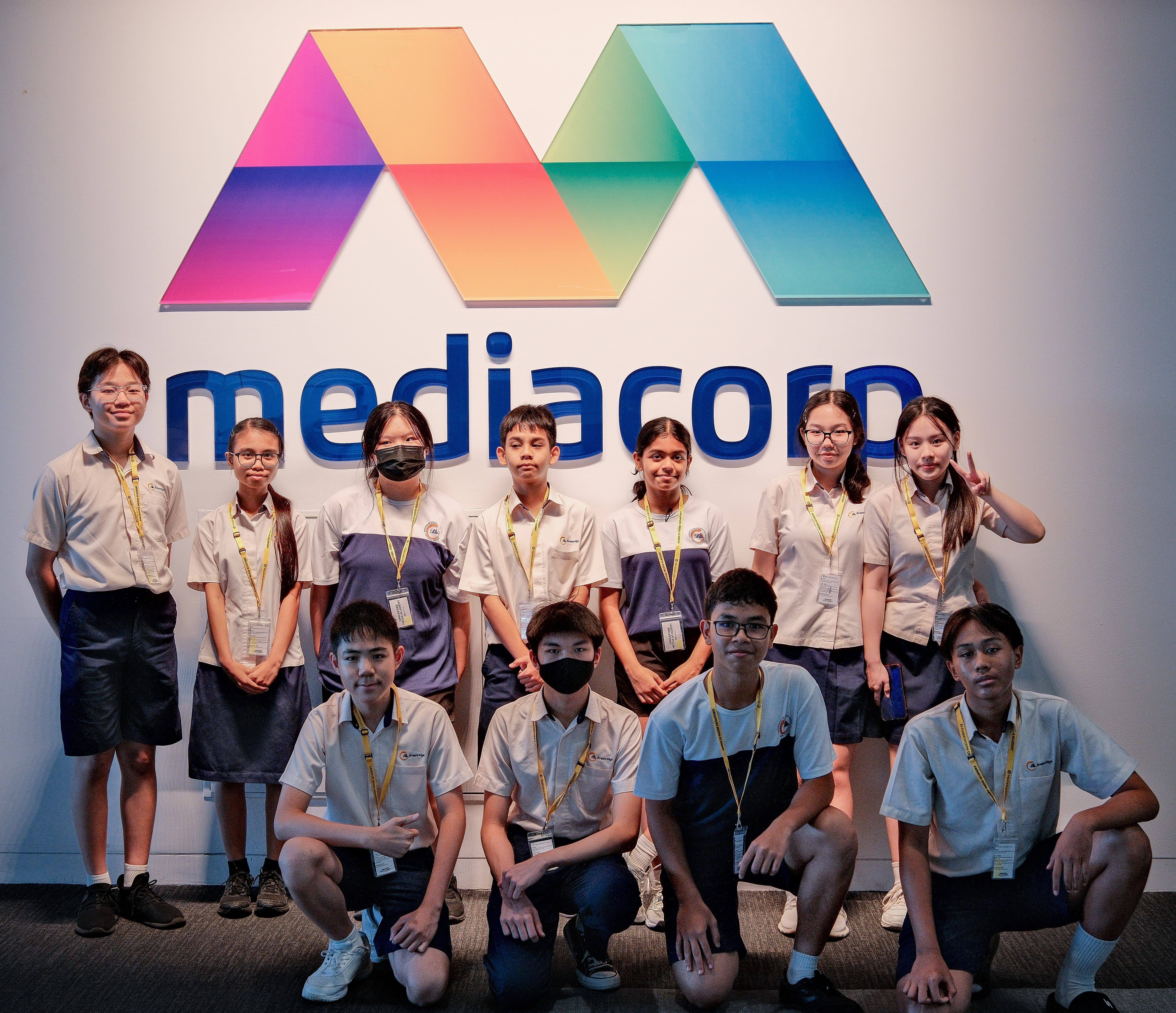 Ten students pose in front of a wall with a colorful M symbol and the word mediacorp in blue.