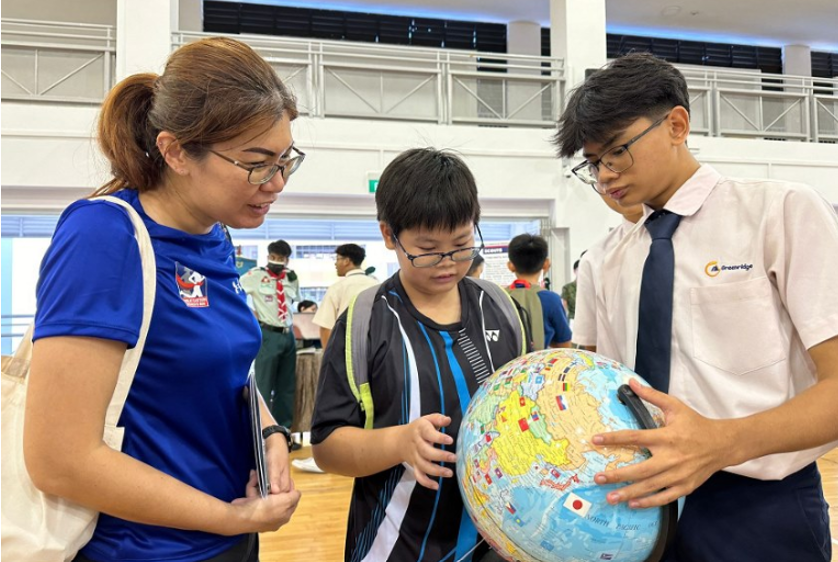 Three people, including two students and an adult woman, examine a world globe together indoors.