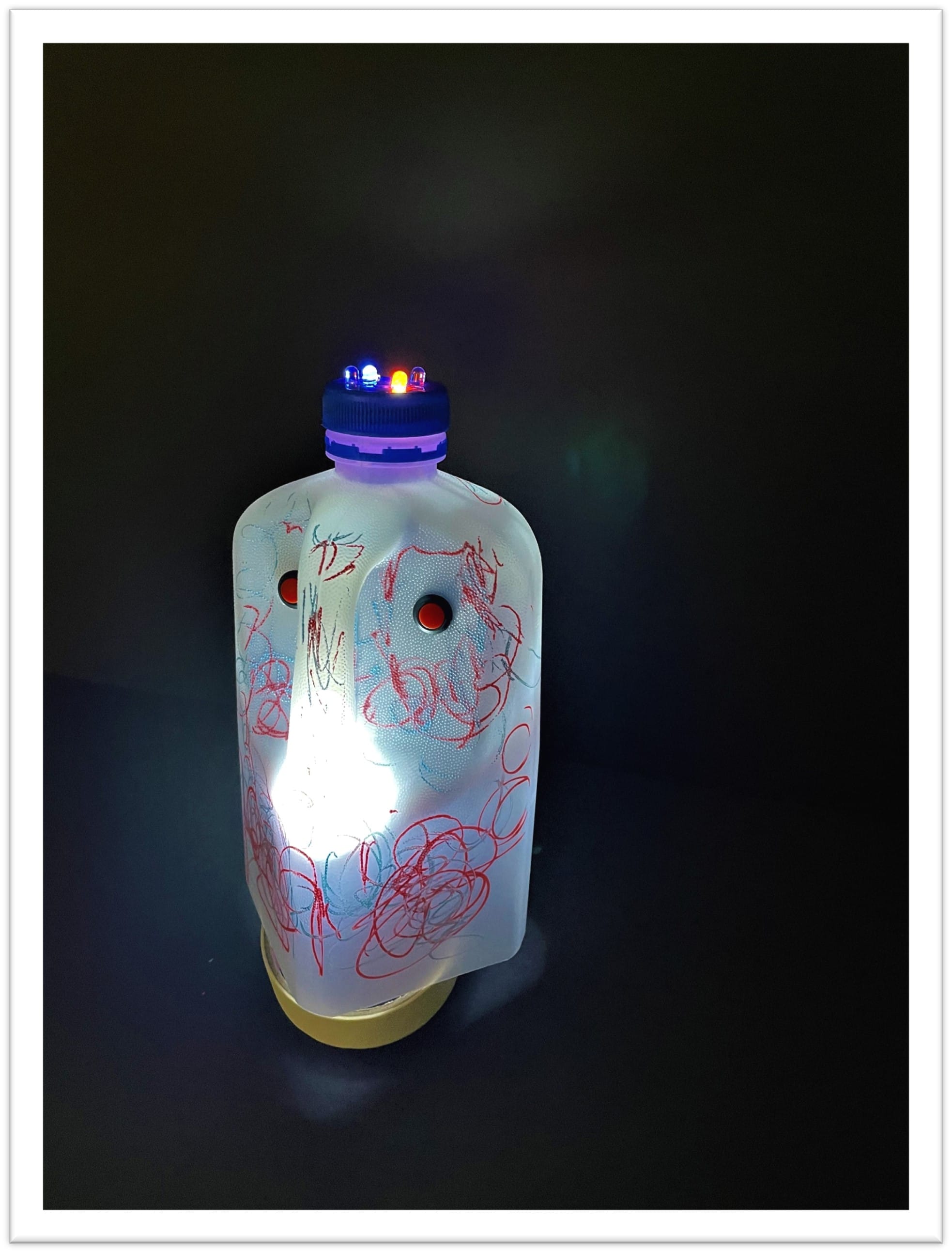 A glowing plastic bottle covered in red and blue scribbles, with small LED lights on top, against a dark background.