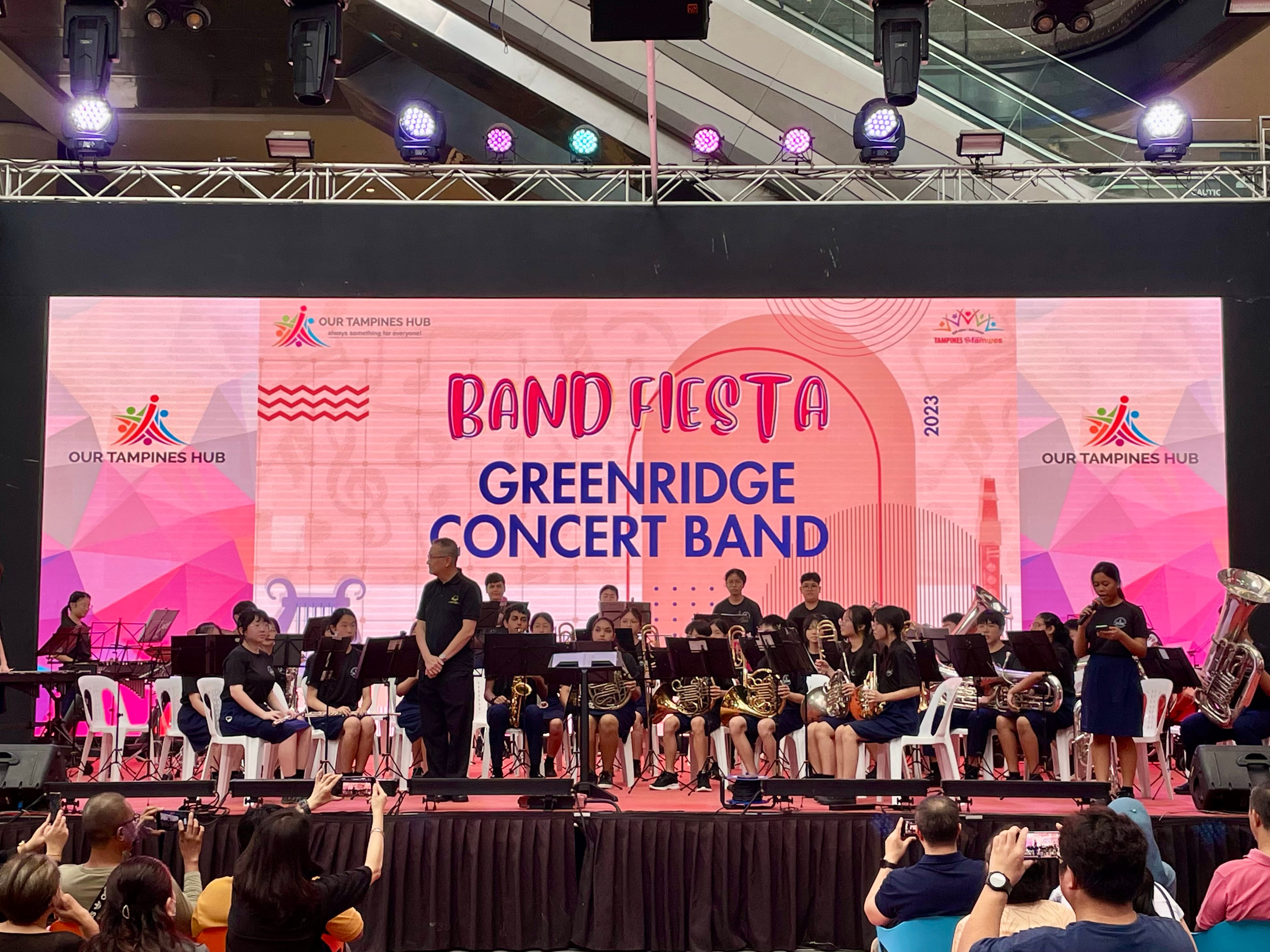 Greenridge Concert Band students perform on stage at Band Fiesta 2023 at Our Tampines Hub, with audience watching.