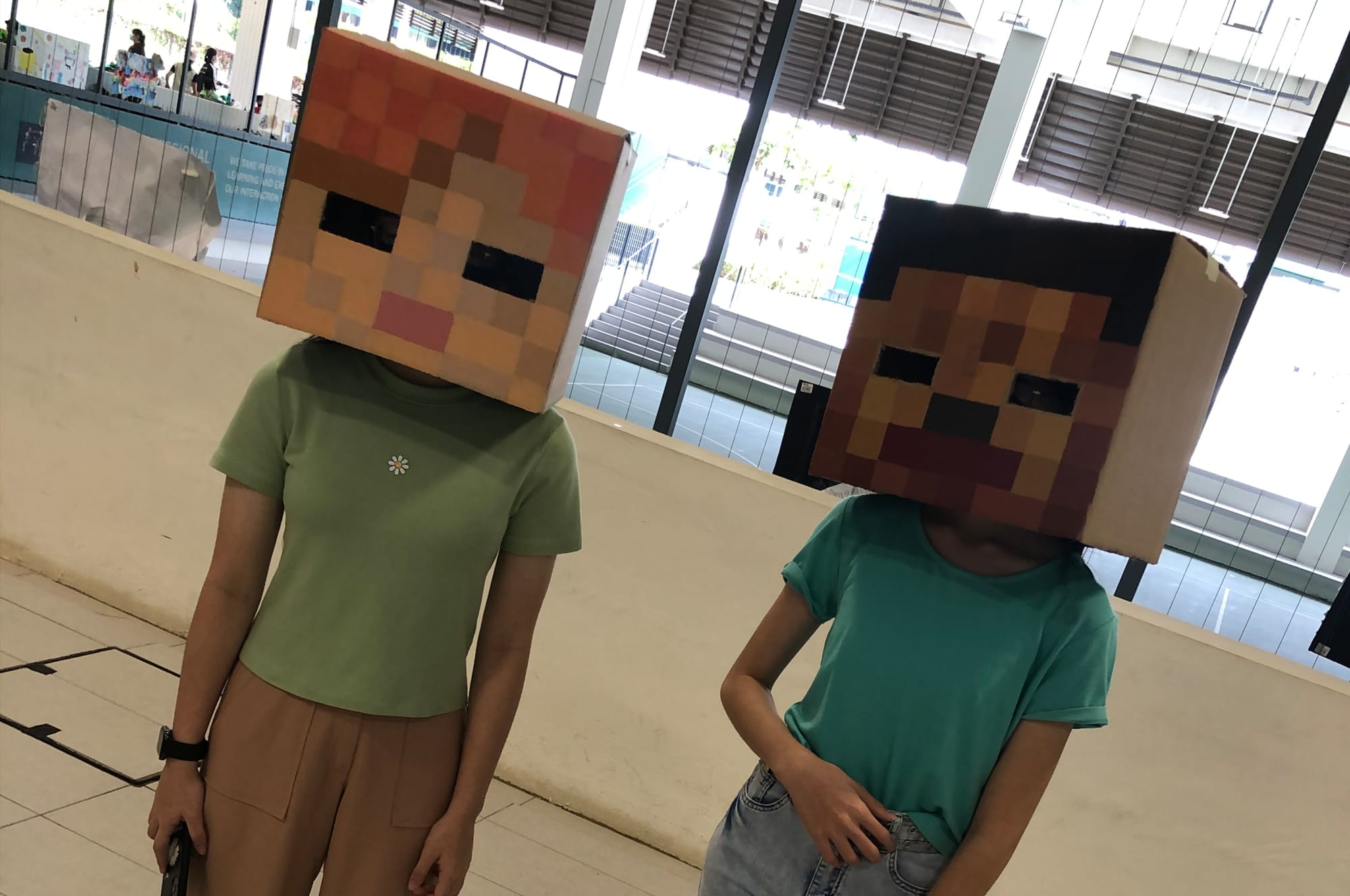 Two people wearing cardboard Minecraft character head costumes, one in a green shirt and one in a teal shirt.
