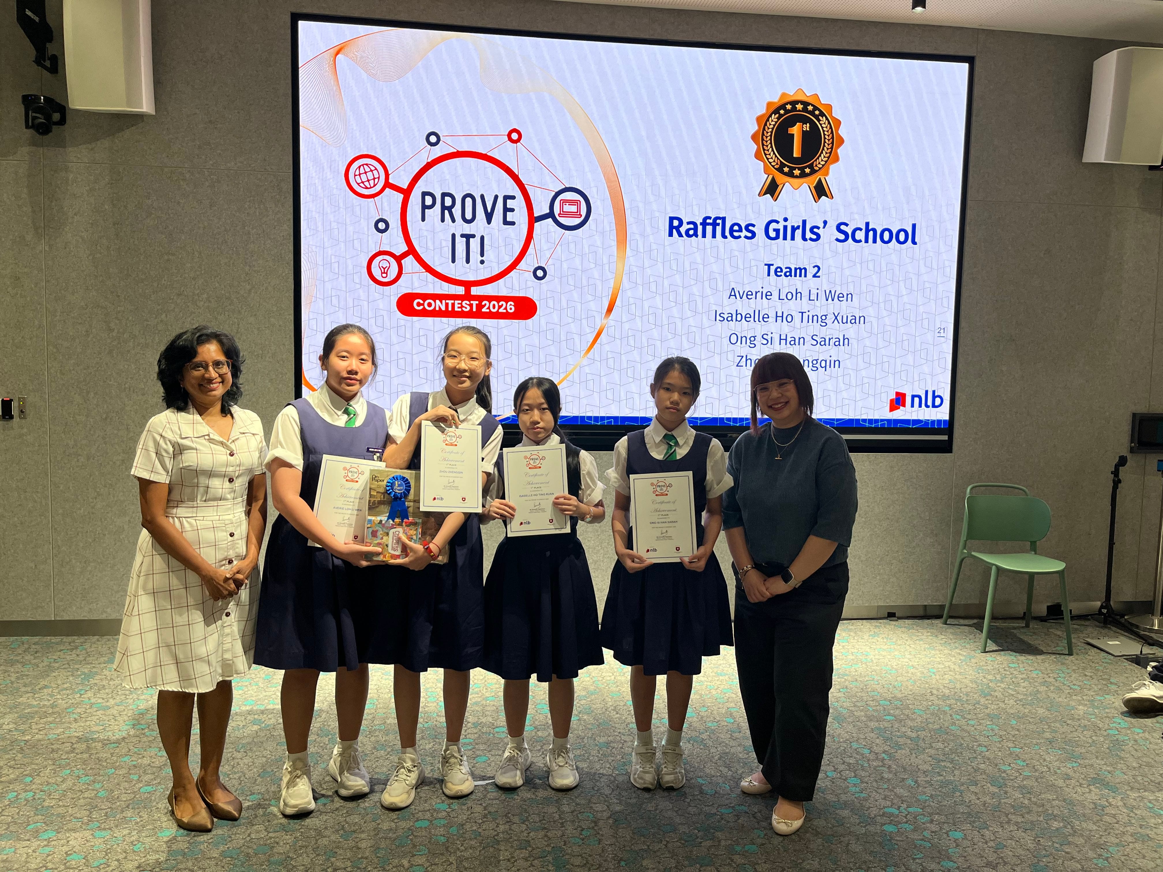 A group photo of female students holding their award certificate and and two female prize presenters, standing in front of a projected screen stating "Prove It! Contest 2026".