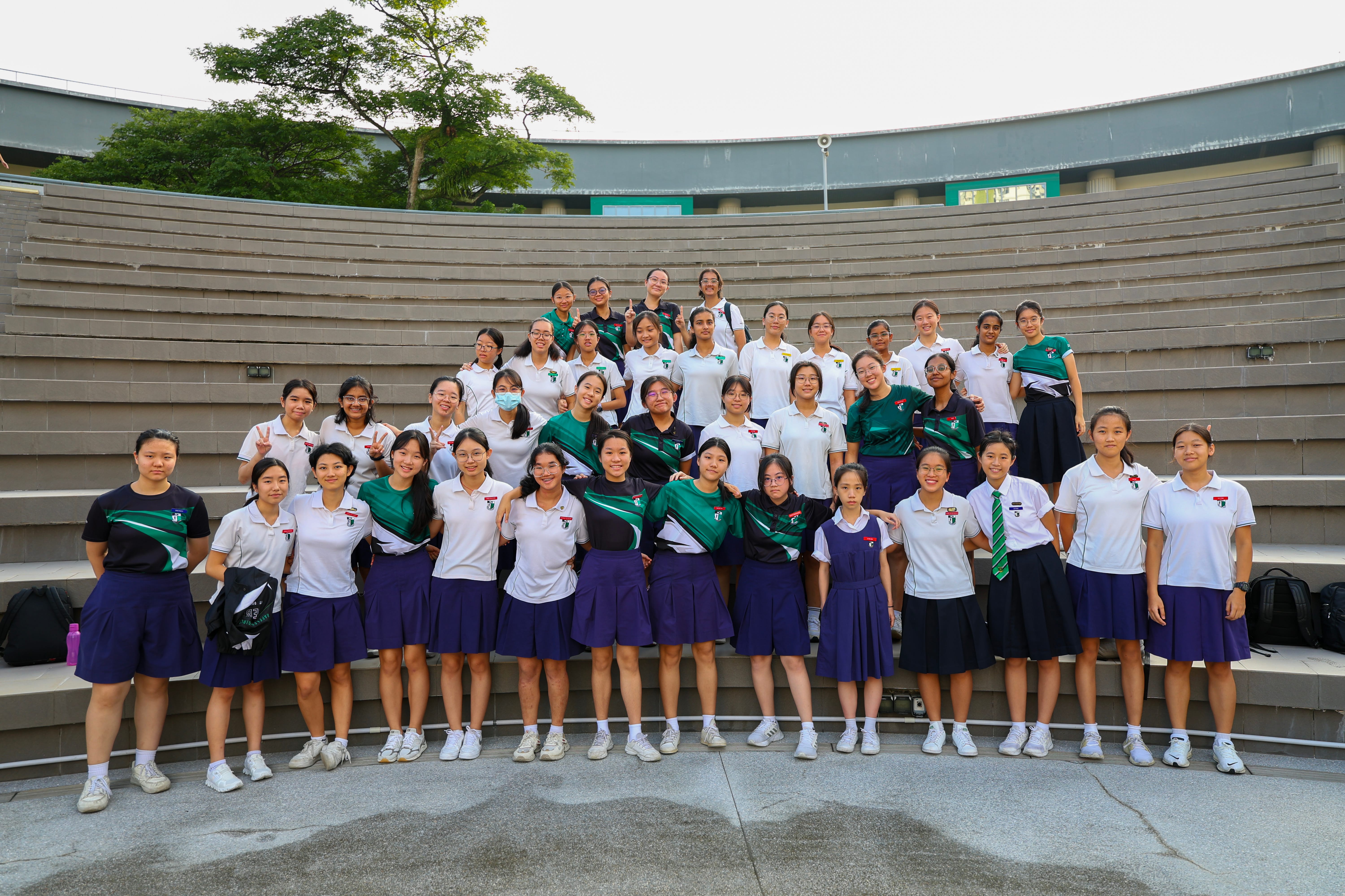 Group of students in school uniforms posing on outdoor amphitheater steps, smiling and posing for the photo..
