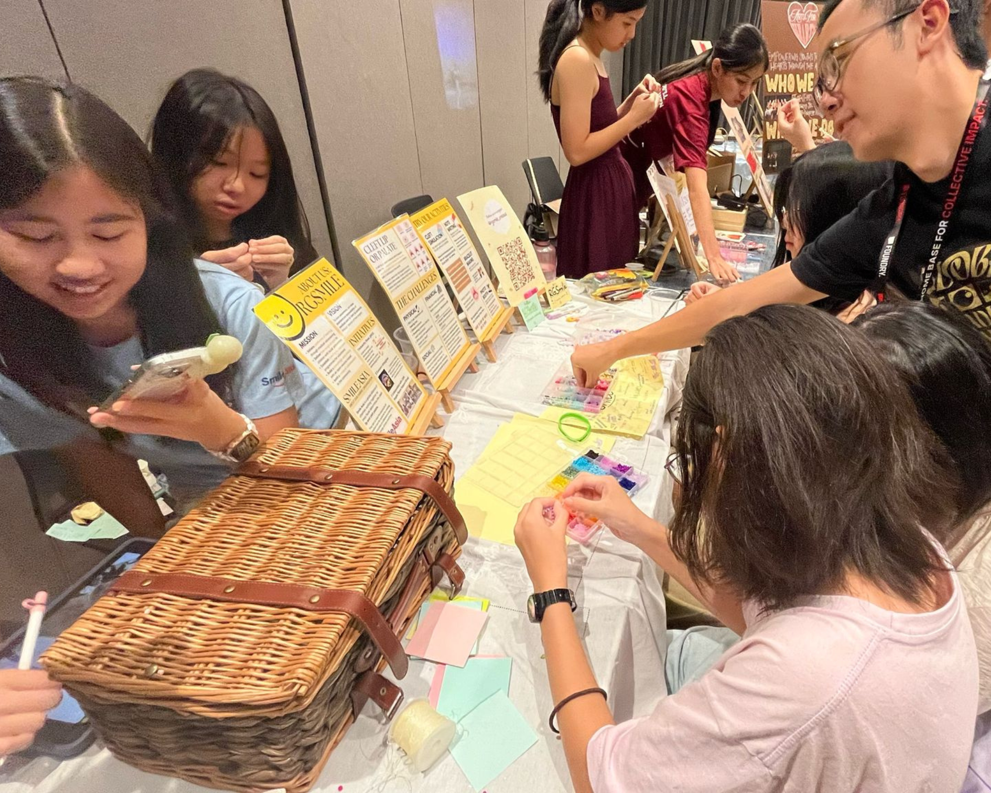 People gathered around a table making crafts, with posters on easels and a wicker picnic basket in front.