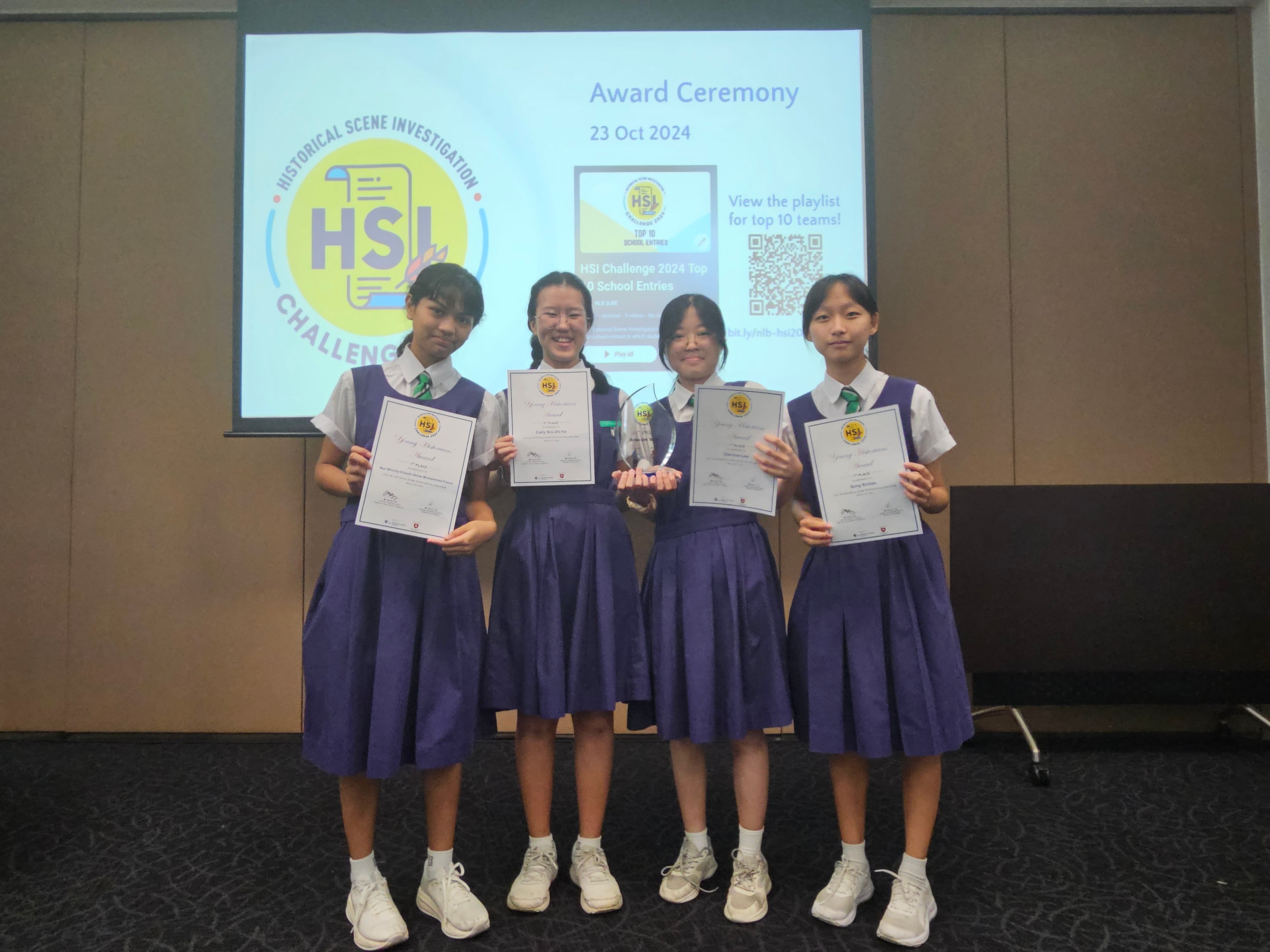Four schoolgirls in purple uniforms hold certificates and a trophy at the HSI Challenge Award Ceremony on 23 Oct 2024.