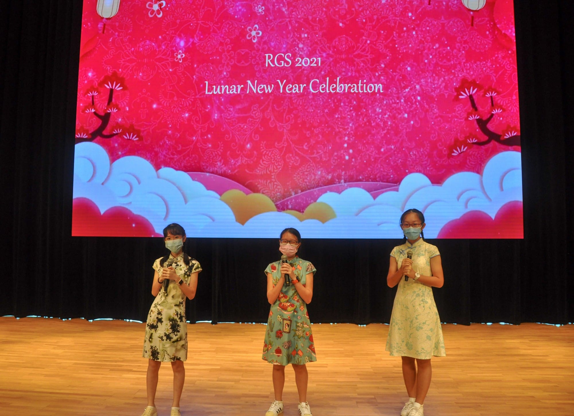 Three girls in traditional dresses holding microphones on stage at RGS 2021 Lunar New Year Celebration.
