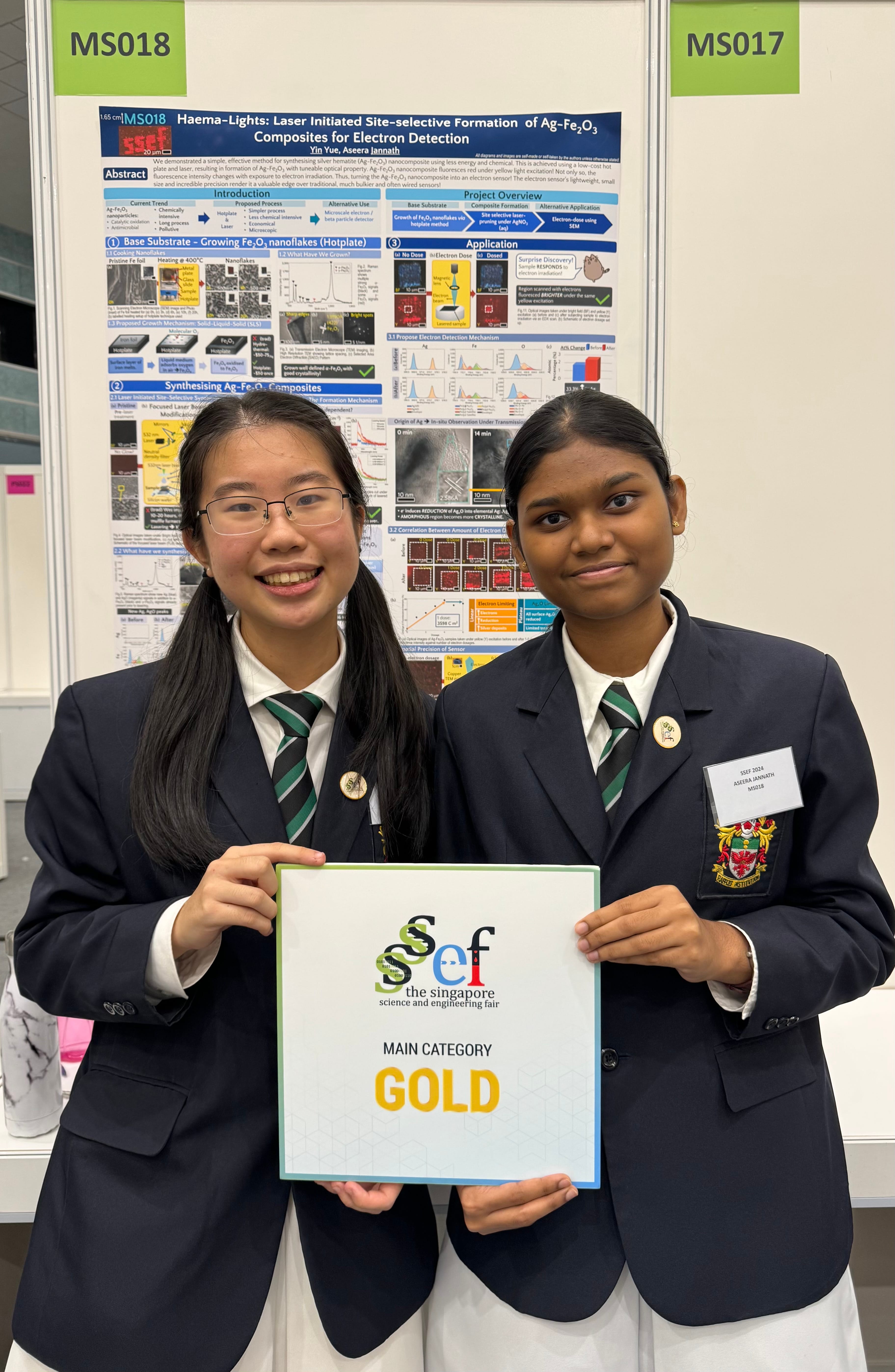 Two students in school uniforms holding a Singapore Science and Engineering Fair Main Category Gold award sign.
