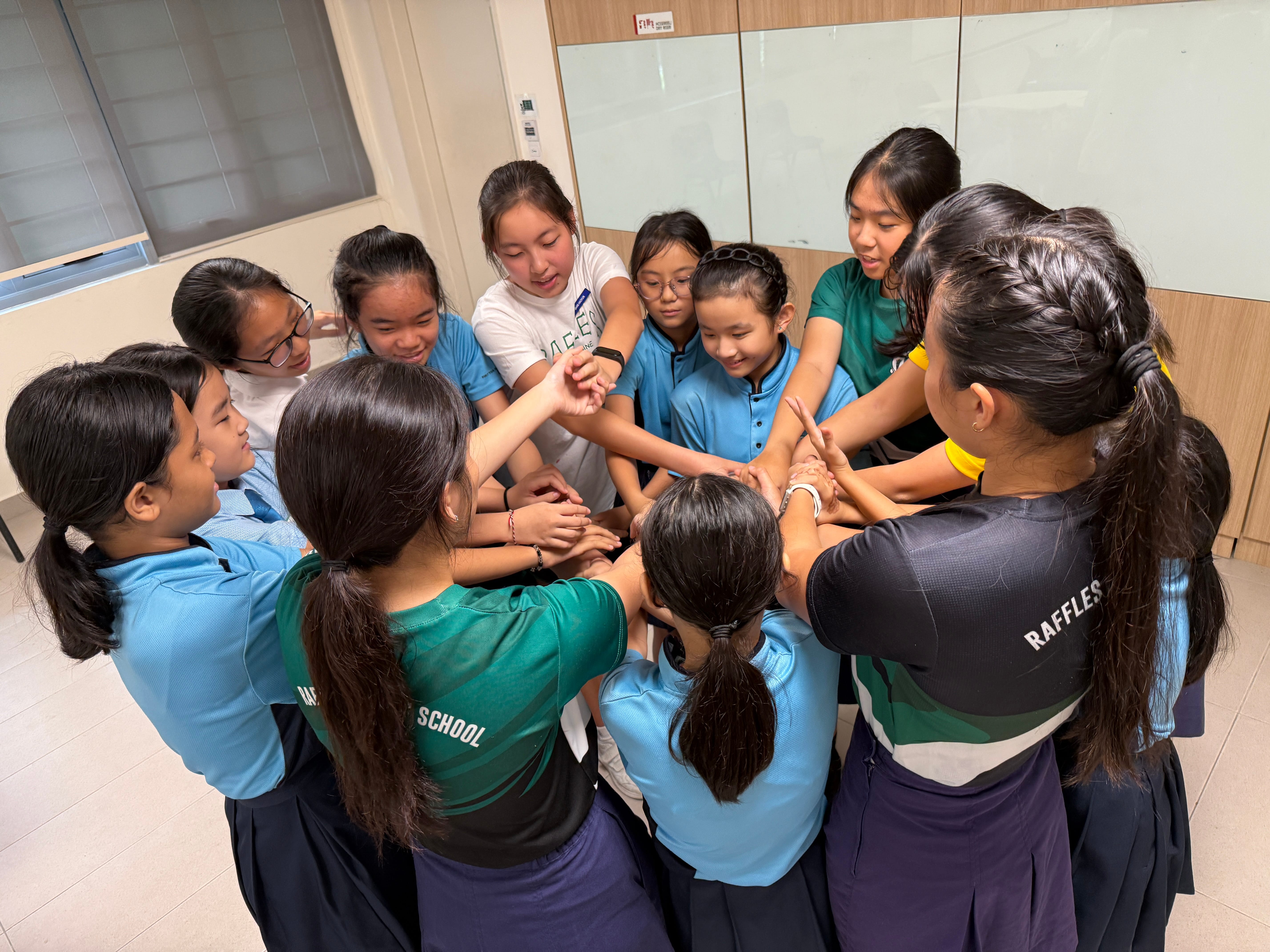 Group of schoolgirls in uniforms standing in a circle with hands stacked together in the center.